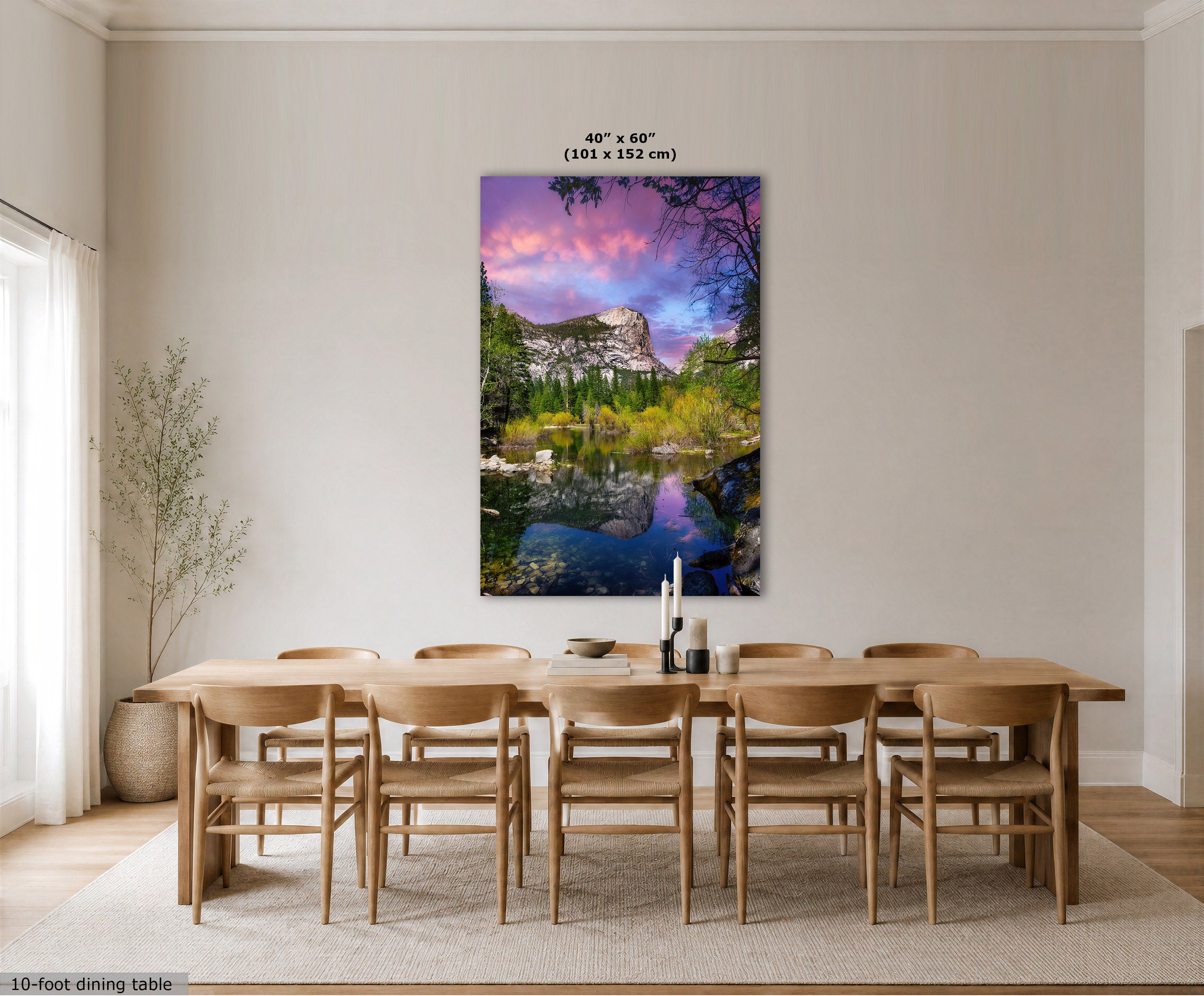 A large vertical canvas wall art print depicting a colorful mountain lake landscape with pink and purple sky, shown hanging above a wooden dining table and chairs in a bright modern room. Text at the top indicates 40 x 60 inches, and text at the bottom left says 10-foot dining table.