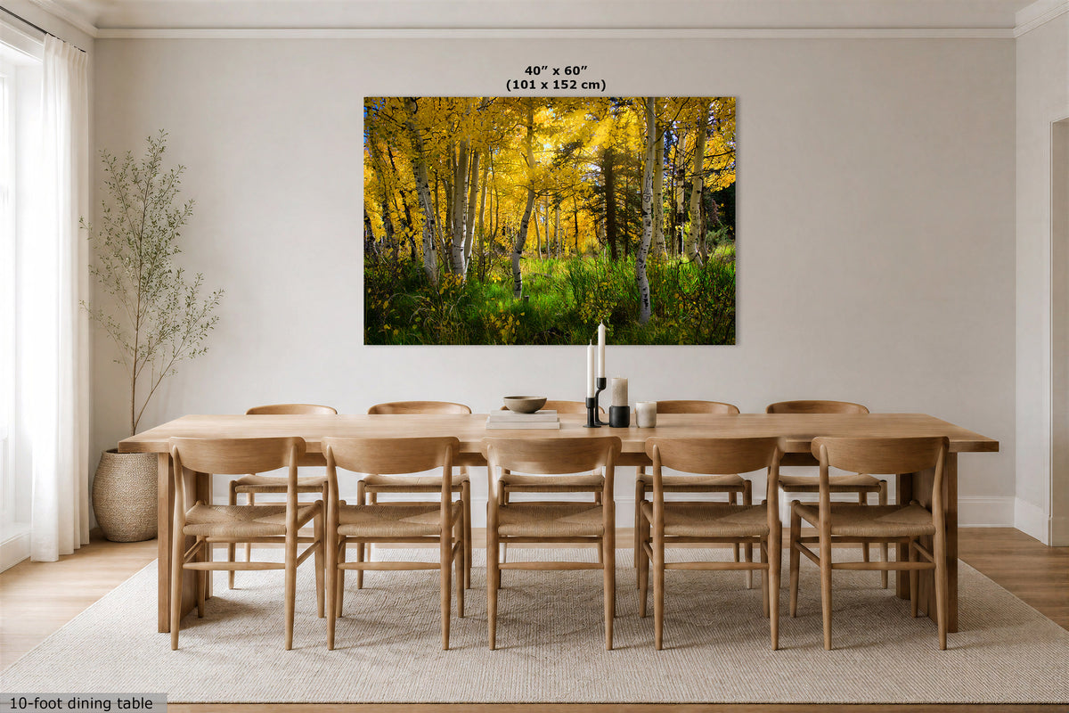 A large wall art print showing a golden autumn forest with yellow trees and green undergrowth, displayed above a wooden dining table and chairs in a bright neutral dining room. Text at the top reads 40" x 60" (101 x 152 cm).