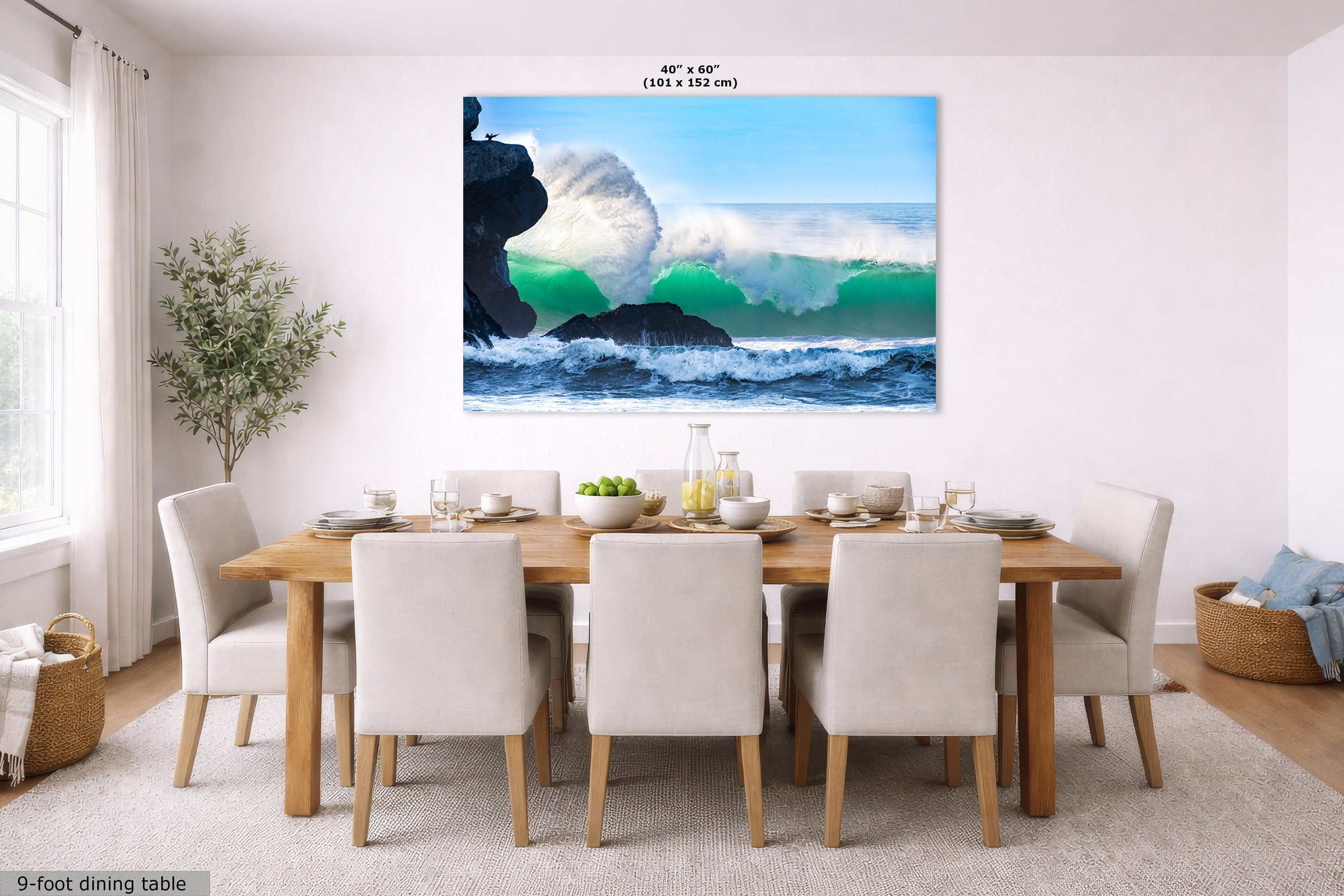 A large rectangular wall art print showing a green ocean wave crashing over dark rocks, displayed above a wooden dining table with white chairs in a bright dining room. The print includes size text at the top and a small label in the corner.