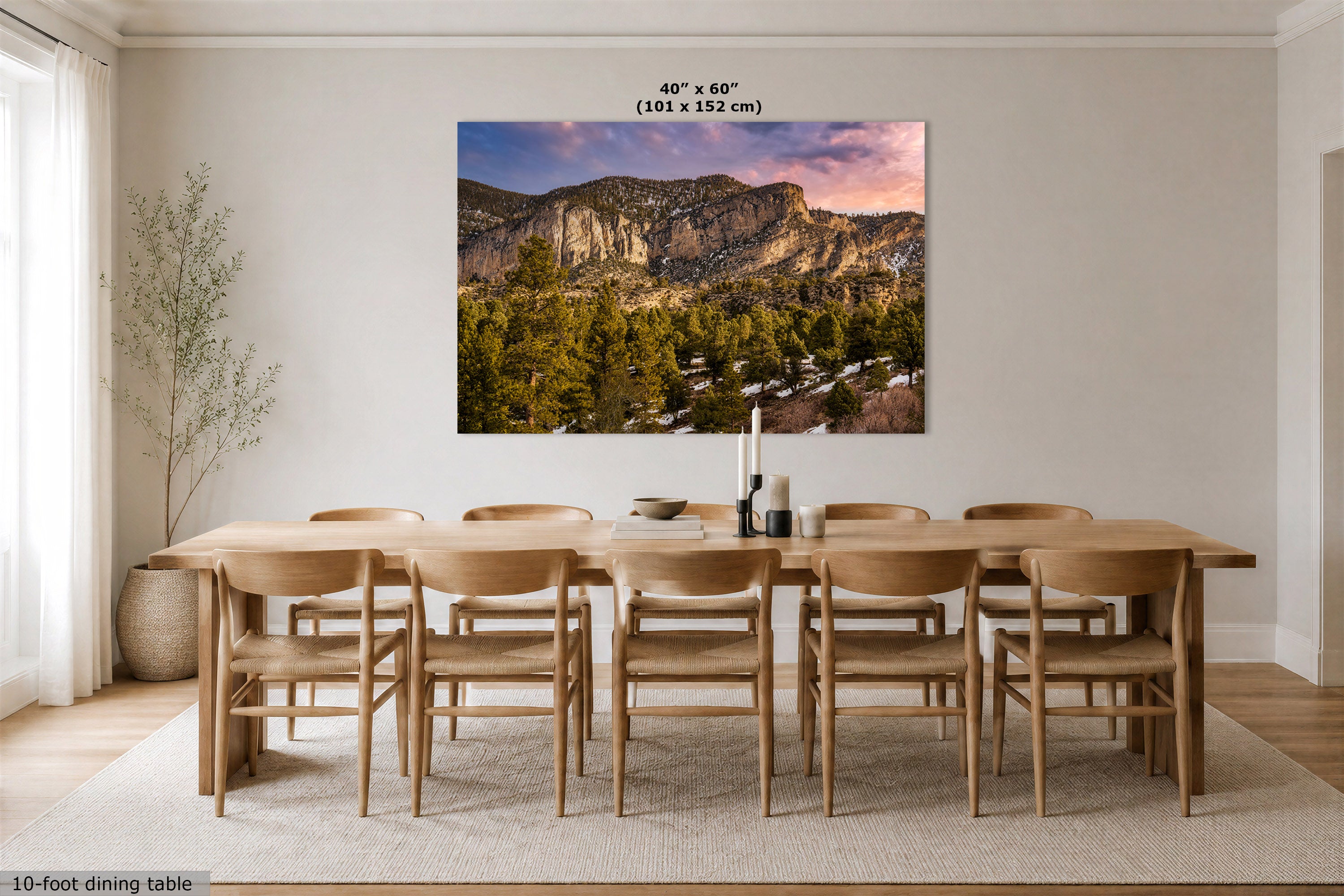 A large rectangular wall art print showing a mountain landscape at sunset hangs above a wooden dining table and chairs in a bright, modern dining room. The print includes size text at the top reading 40" x 60" (102 x 152 cm).