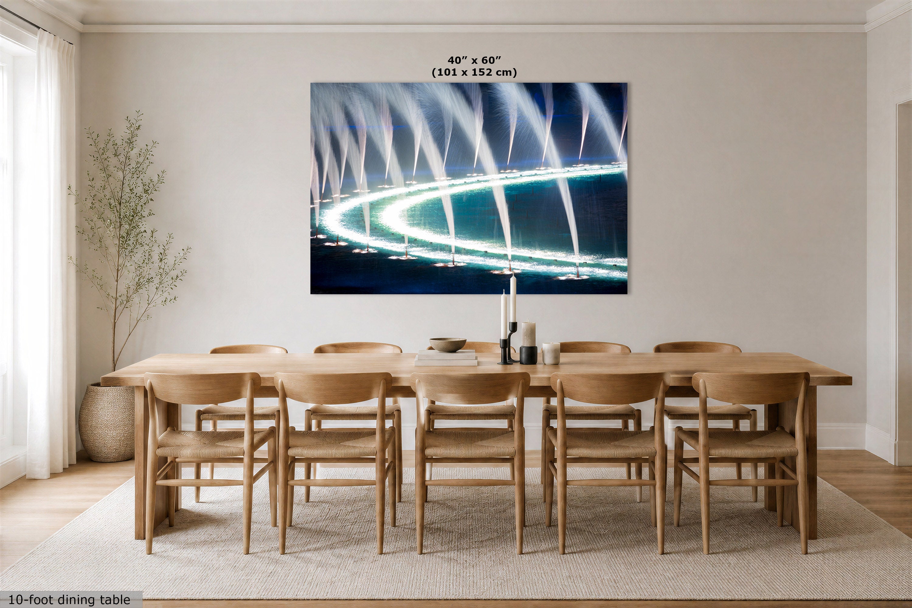 A large rectangular wall art print showing a glowing curved fountain or light display over dark water, displayed above a wooden dining table and chairs in a bright neutral dining room. The print includes size text at the top: 40” x 60” (101 x 152 cm).