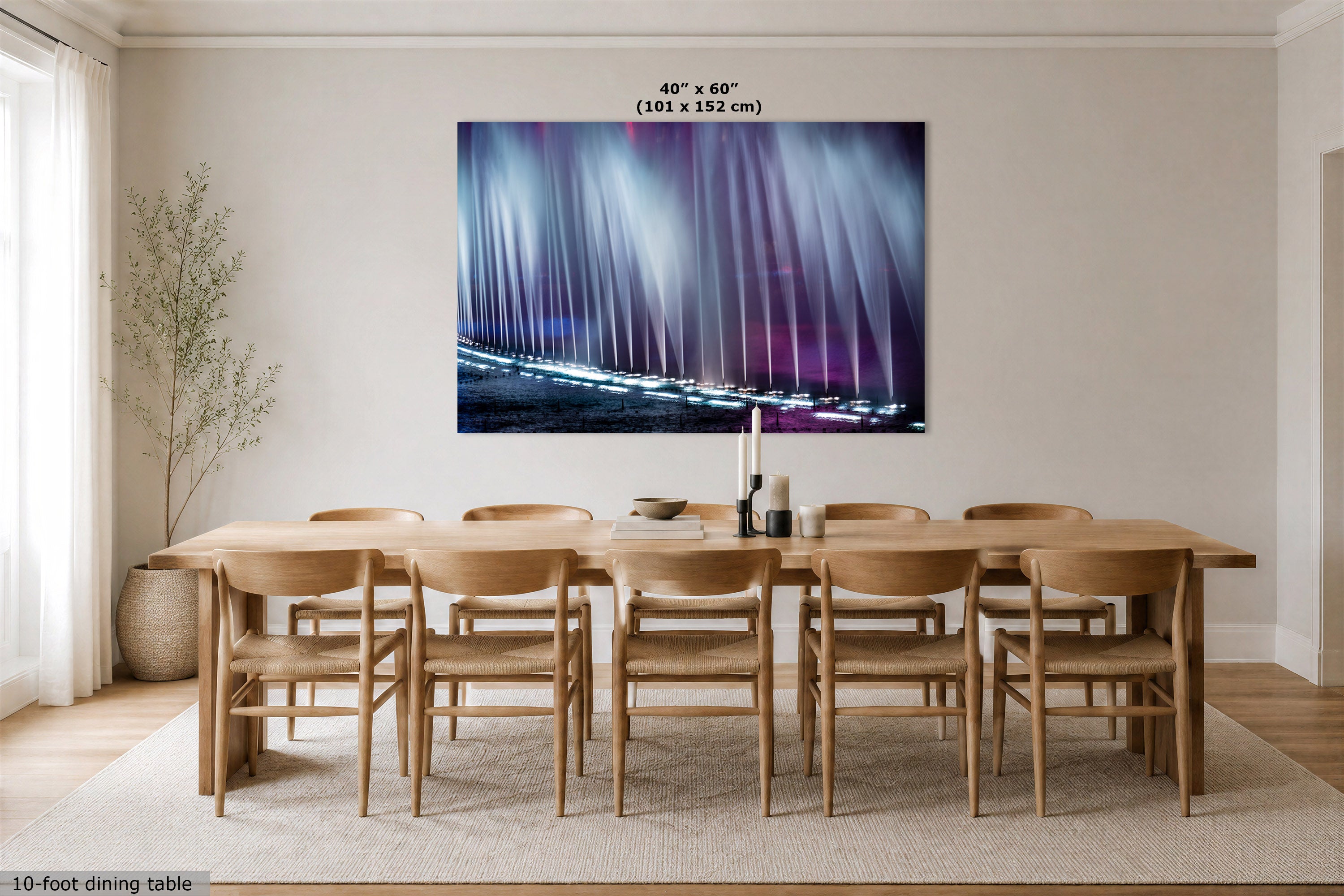 A large abstract fountain wall art print showing vertical light streaks in blue, purple, and pink tones, displayed above a wooden dining table and chairs in a bright neutral dining room. Text at the top of the print reads 40" x 60" (101 x 152 cm), and small text at the bottom left says 10-foot dining table.