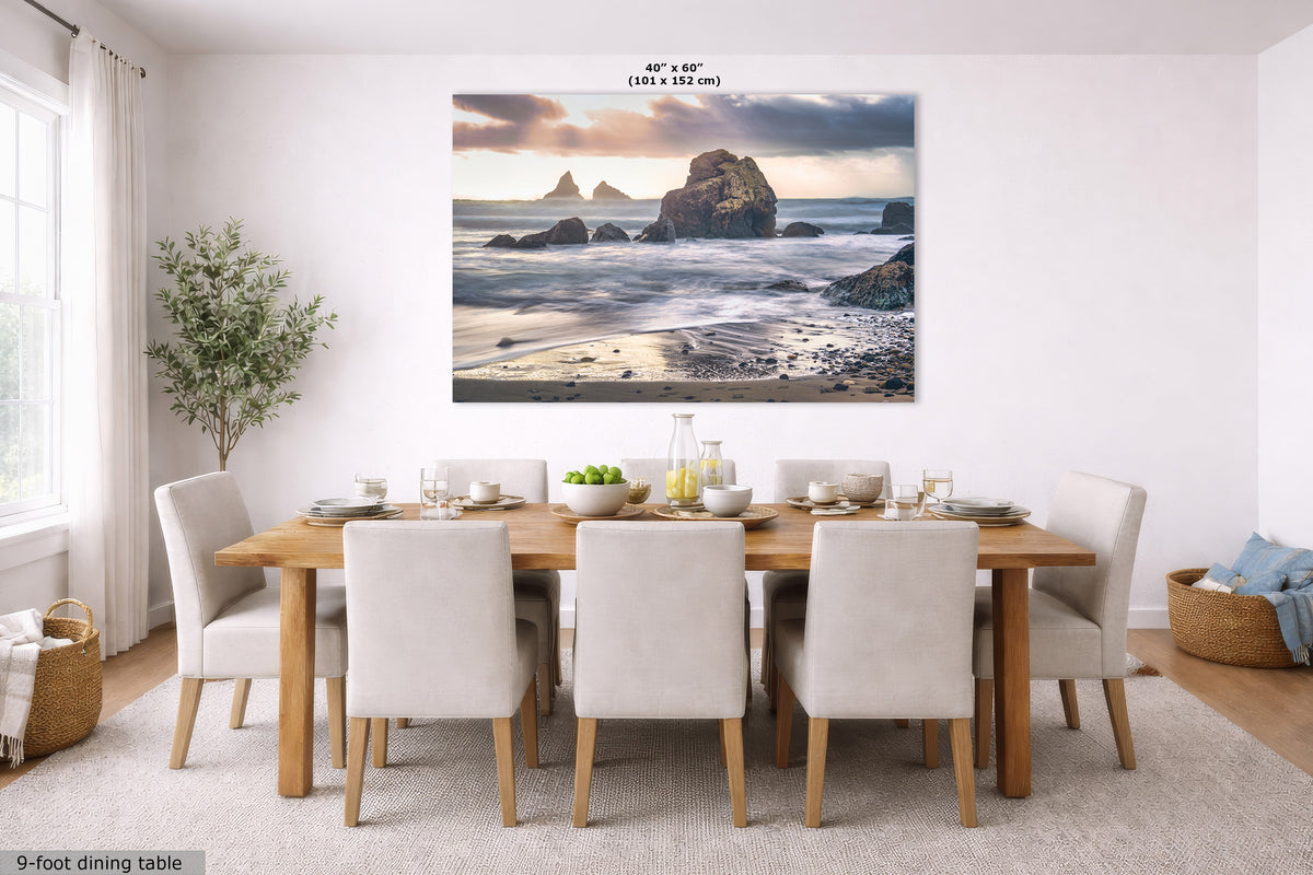 A large rectangular wall art print showing a coastal rock formation at sunset, displayed above a wooden dining table with white upholstered chairs in a bright modern dining room. The print has a small size label reading 40" x 60" (101 x 152 in) at the top.