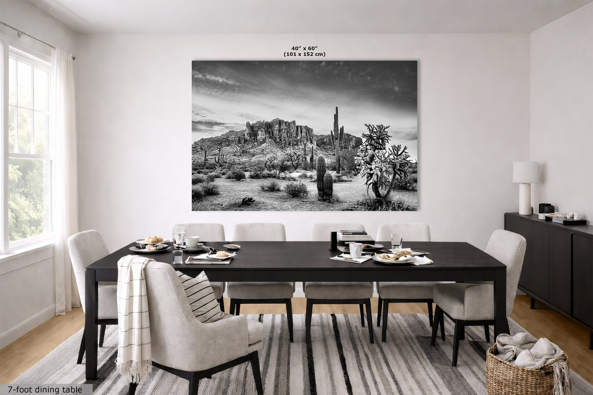 A large black and white landscape wall art print depicting a desert canyon scene with cacti, hung above a dark dining table in a modern dining room. The print includes size text at the top reading 40 in x 60 in.