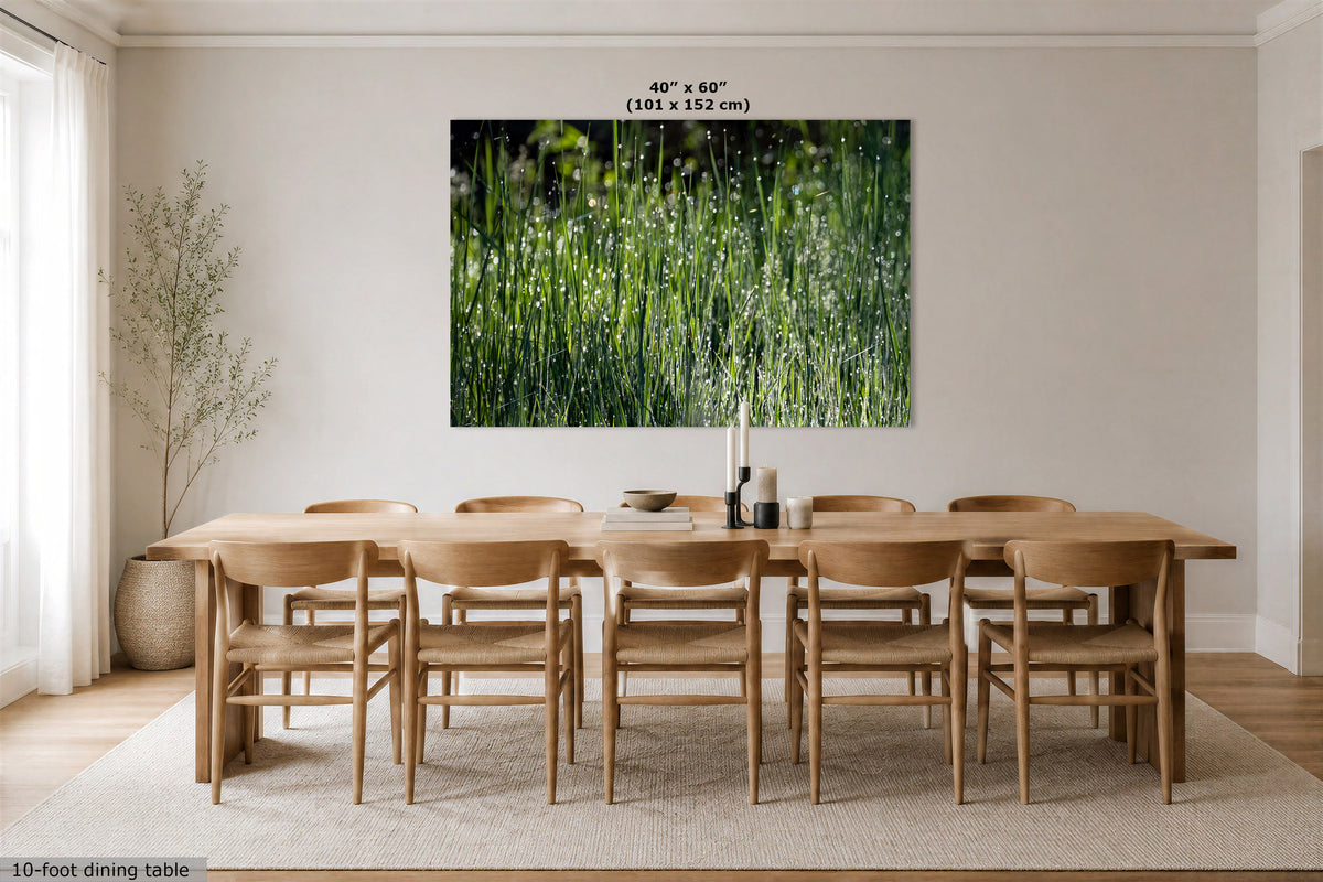 A large wall art print showing a green grassy field hangs above a light wood dining table and chairs in a bright neutral dining room. Text at the top of the print reads 40" x 60" (101 x 152 cm), and a small caption at the bottom left says 10-foot dining table.