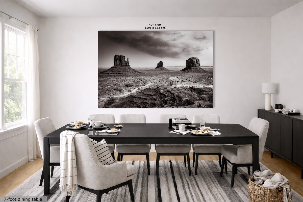 A large black and white landscape wall art print depicting desert rock formations, displayed in a modern dining room setting above a dark wood dining table and chairs.