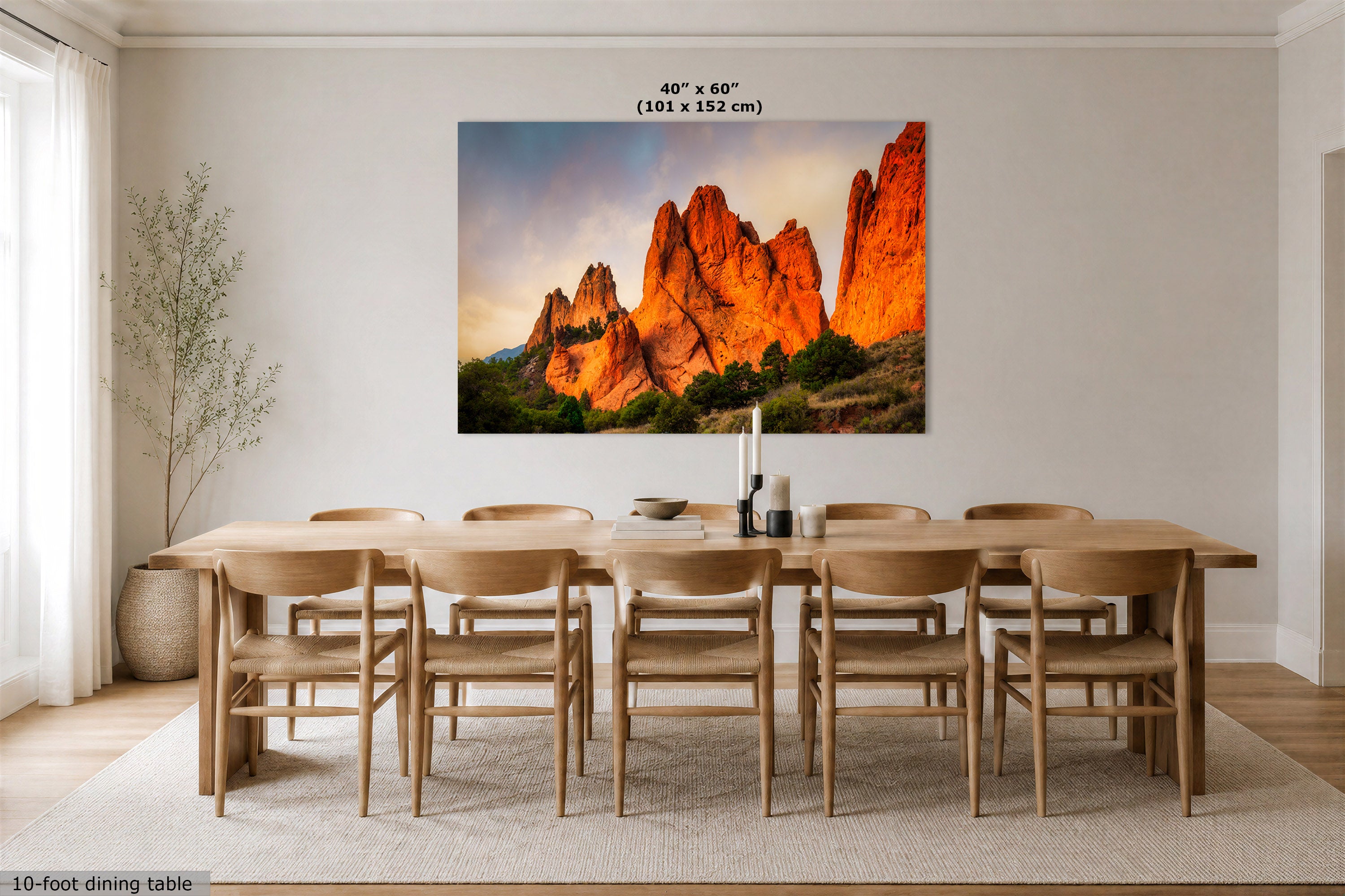 A large rectangular wall art print showing a desert rock formation landscape in warm orange and red tones, displayed above a wooden dining table in a bright neutral dining room. Text at the top reads 40" x 60" (101 x 152 cm), and text at the bottom left reads 10-foot dining table.