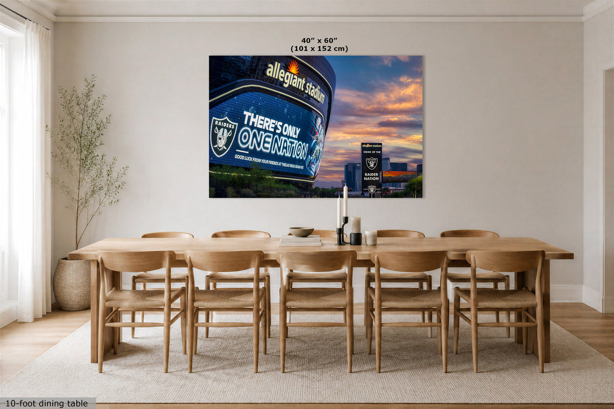 A large wall art print showing the Allegiant Stadium scoreboard at sunset, displayed above a wooden dining table in a bright modern dining room. The print includes size text at the top and a small product label at the bottom left.