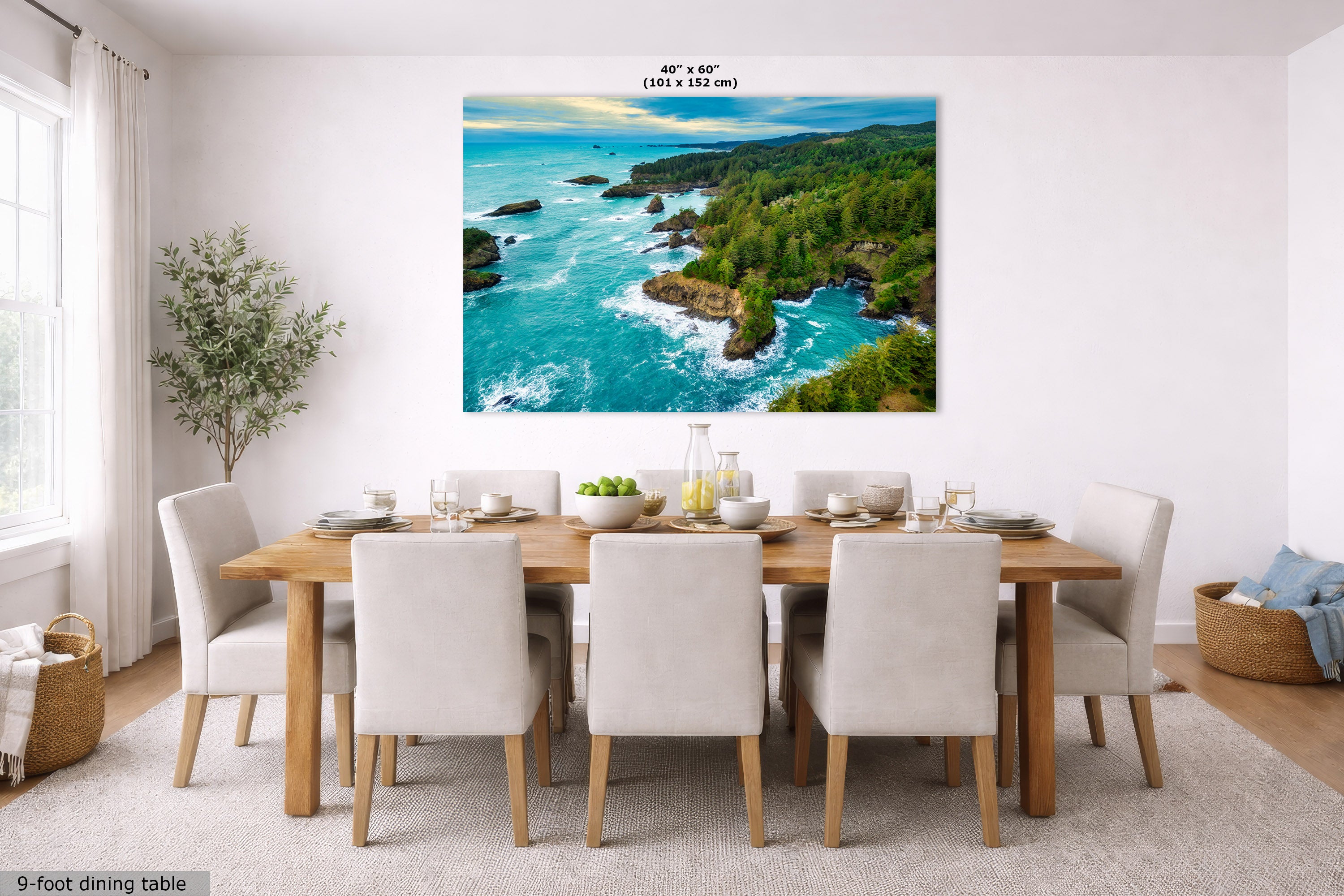 A large wall art print showing a coastal ocean landscape with turquoise water, rocky cliffs, and green forest, displayed above a dining table in a bright modern room. Small text at the top of the print reads 40" x 60".
