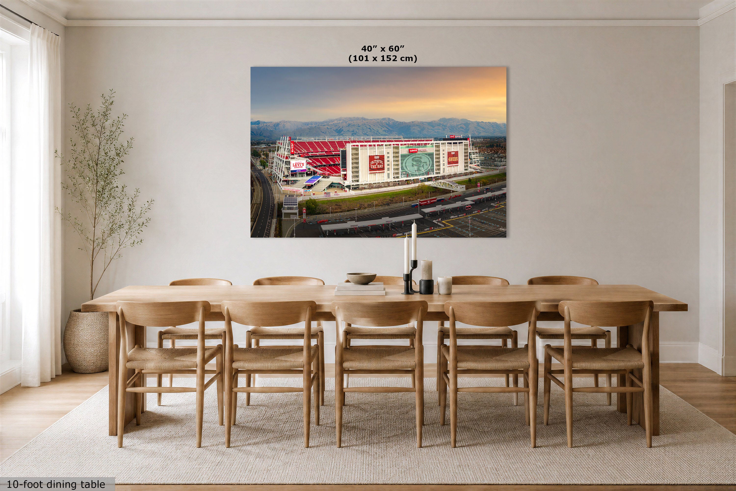 A large wall art print showing an aerial view of a stadium at sunrise, displayed above a wooden dining table in a modern dining room. The print includes the text '40" x 60" (101 x 152 cm)' at the top.