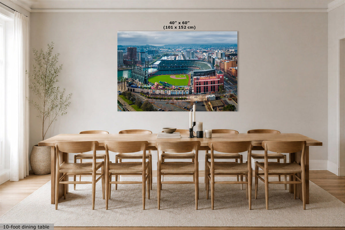 A large wall art print showing an aerial view of a baseball stadium and surrounding cityscape, displayed above a wooden dining table in a bright dining room. The print includes size text at the top reading 40" x 60" (101 x 152 cm).
