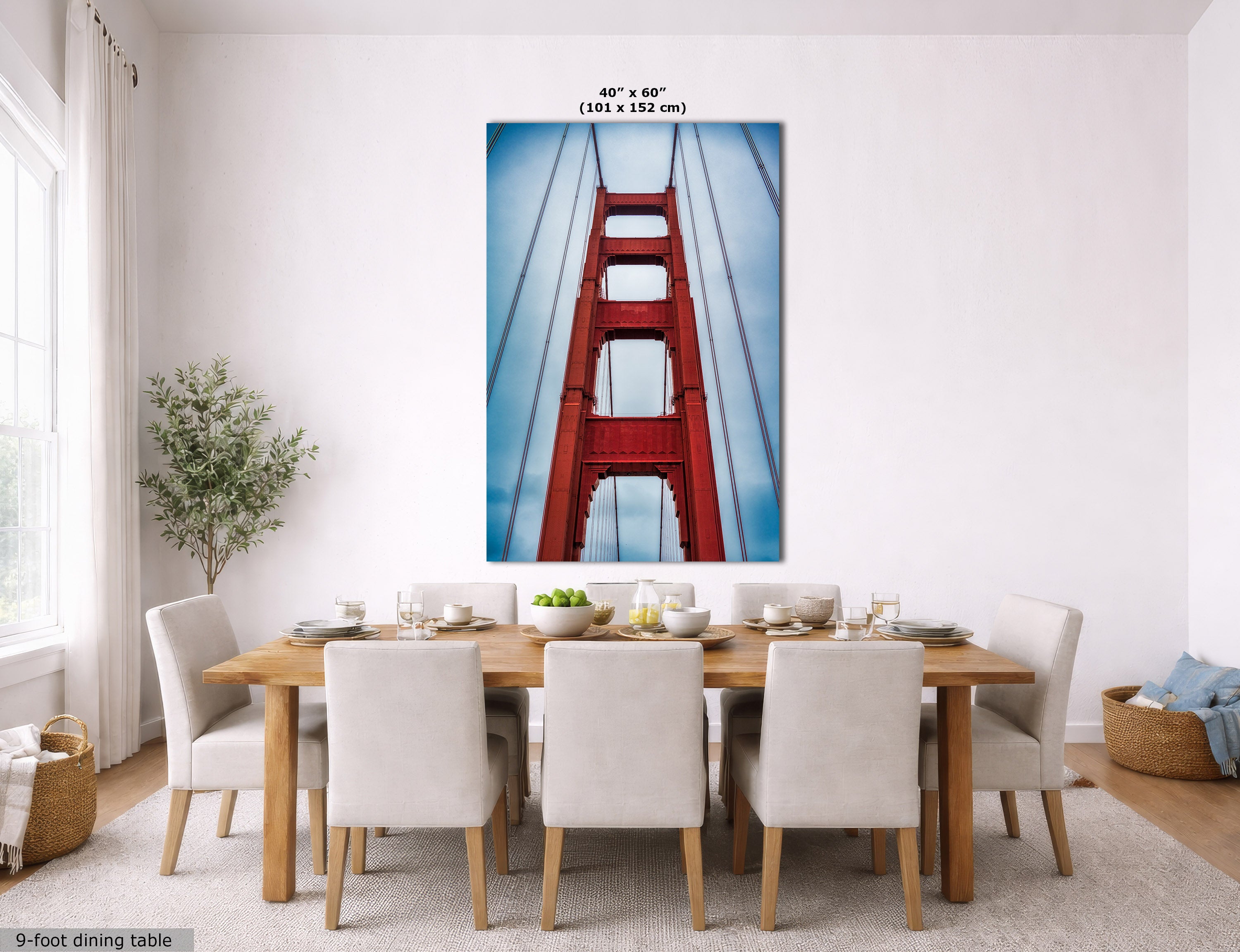 A large vertical wall art print showing a close-up of the Golden Gate Bridge, displayed above a dining table in a bright, modern dining room. The print has a blue sky background with the red bridge structure.