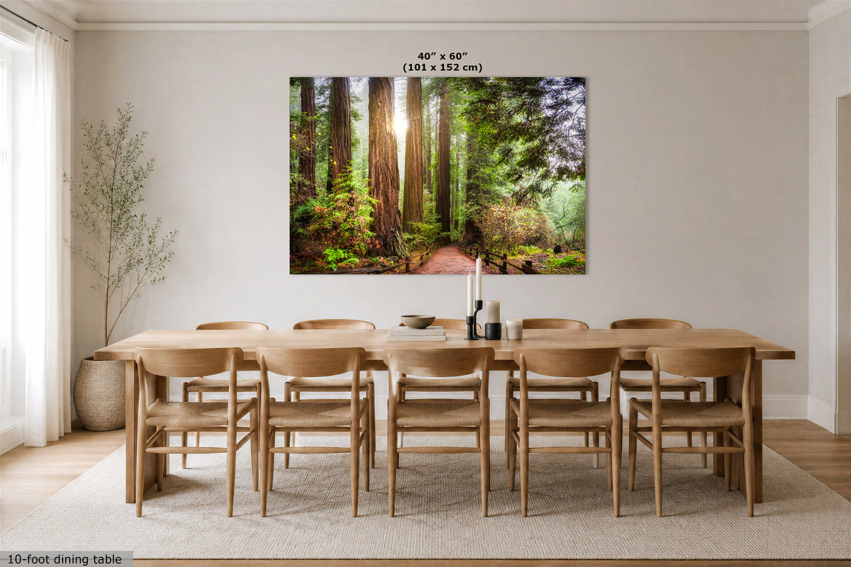 A large rectangular wall art print showing a sunlit forest path with tall trees, displayed above a wooden dining table and chairs in a bright neutral dining room. Text at the top of the print reads 40" x 60" (101 x 152 cm), and small text at the bottom left says 10-foot dining table.