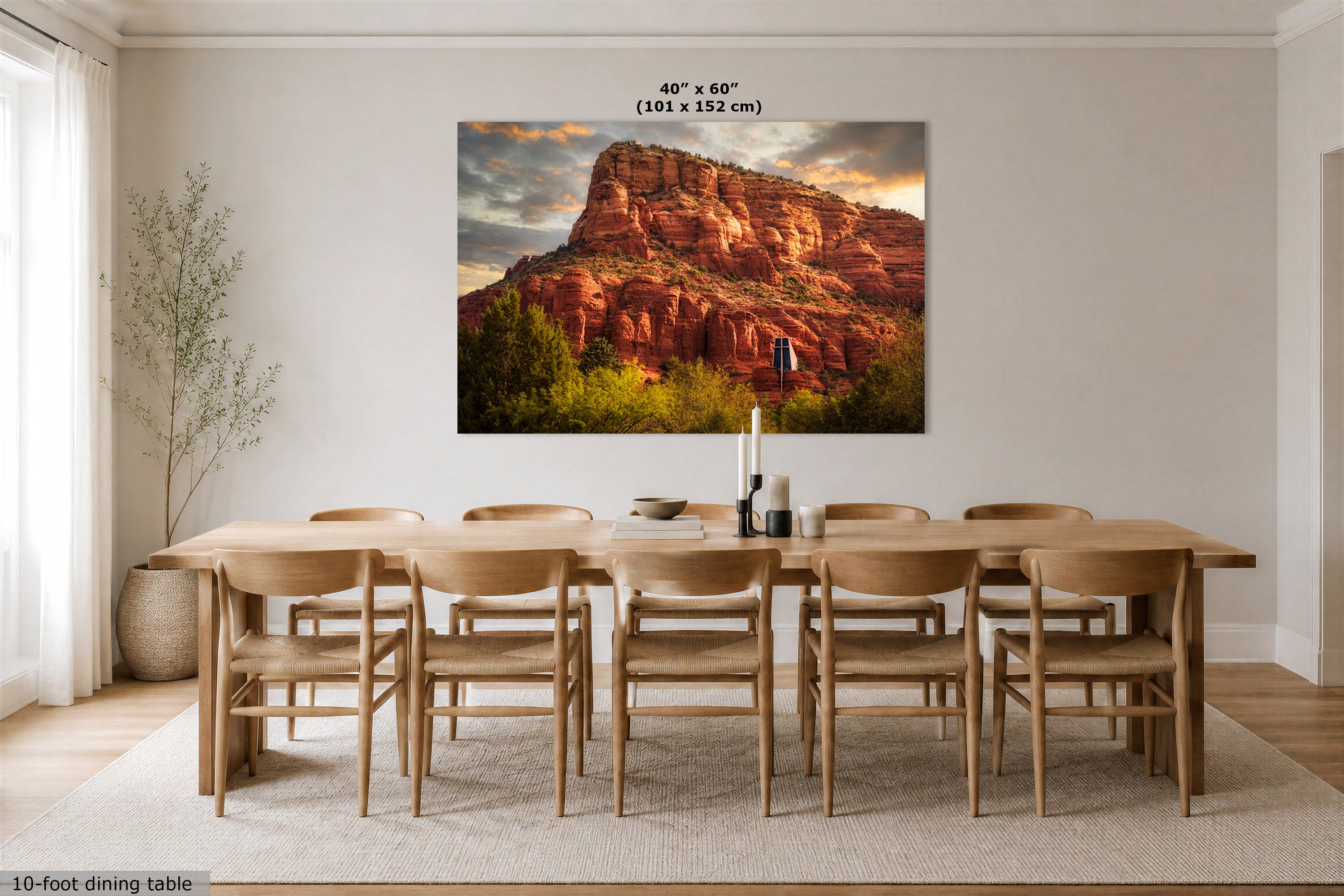 A large rectangular wall art print showing a desert rock landscape in warm orange, red, and brown tones, displayed above a wooden dining table and chairs in a bright neutral dining room. Text at the top reads 40" x 60" (101 x 152 cm), and a small note at bottom left says 10-foot dining table.