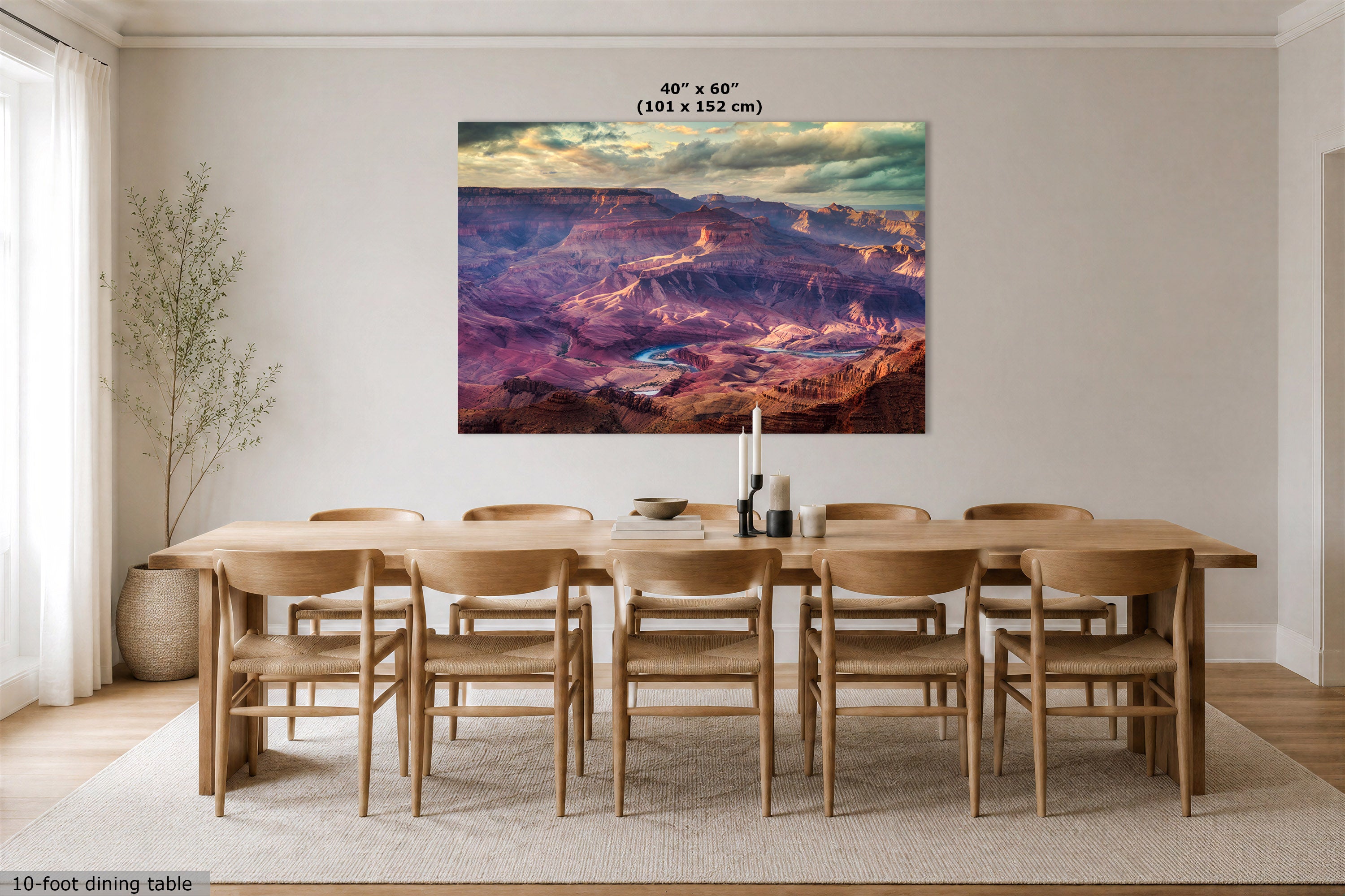 A large wall art print showing a colorful canyon landscape with dramatic clouds, displayed above a wooden dining table and chairs in a bright dining room. Text at the top reads 40" x 60" (101 x 152 cm), and a small note at bottom left says 10-foot dining table.