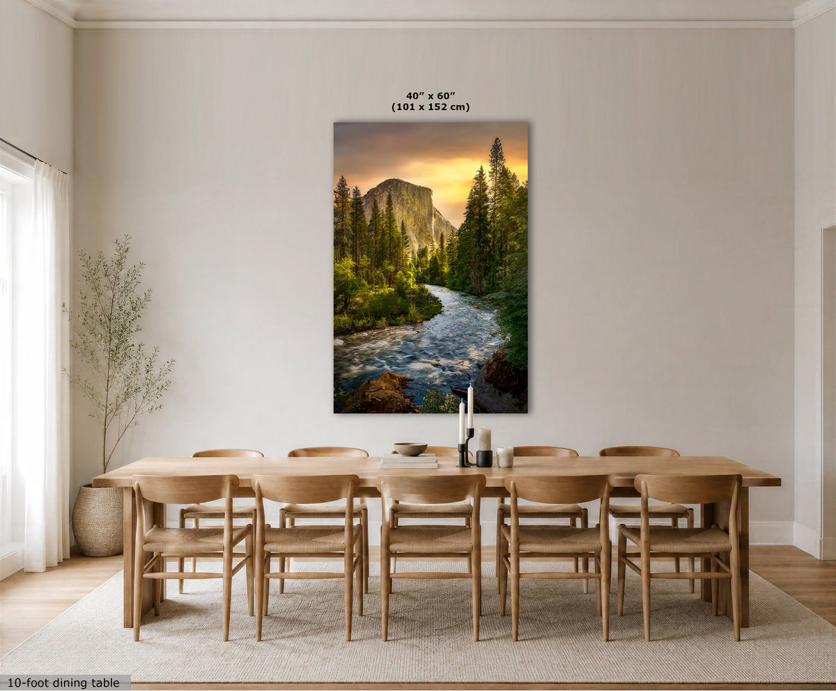 A large vertical canvas print of a mountain and river landscape hangs on a light beige wall above a wooden dining table and chairs in a modern dining room. The print shows a glowing sunset over green forest and water, with text above indicating 40" x 60" (101 x 152 cm).