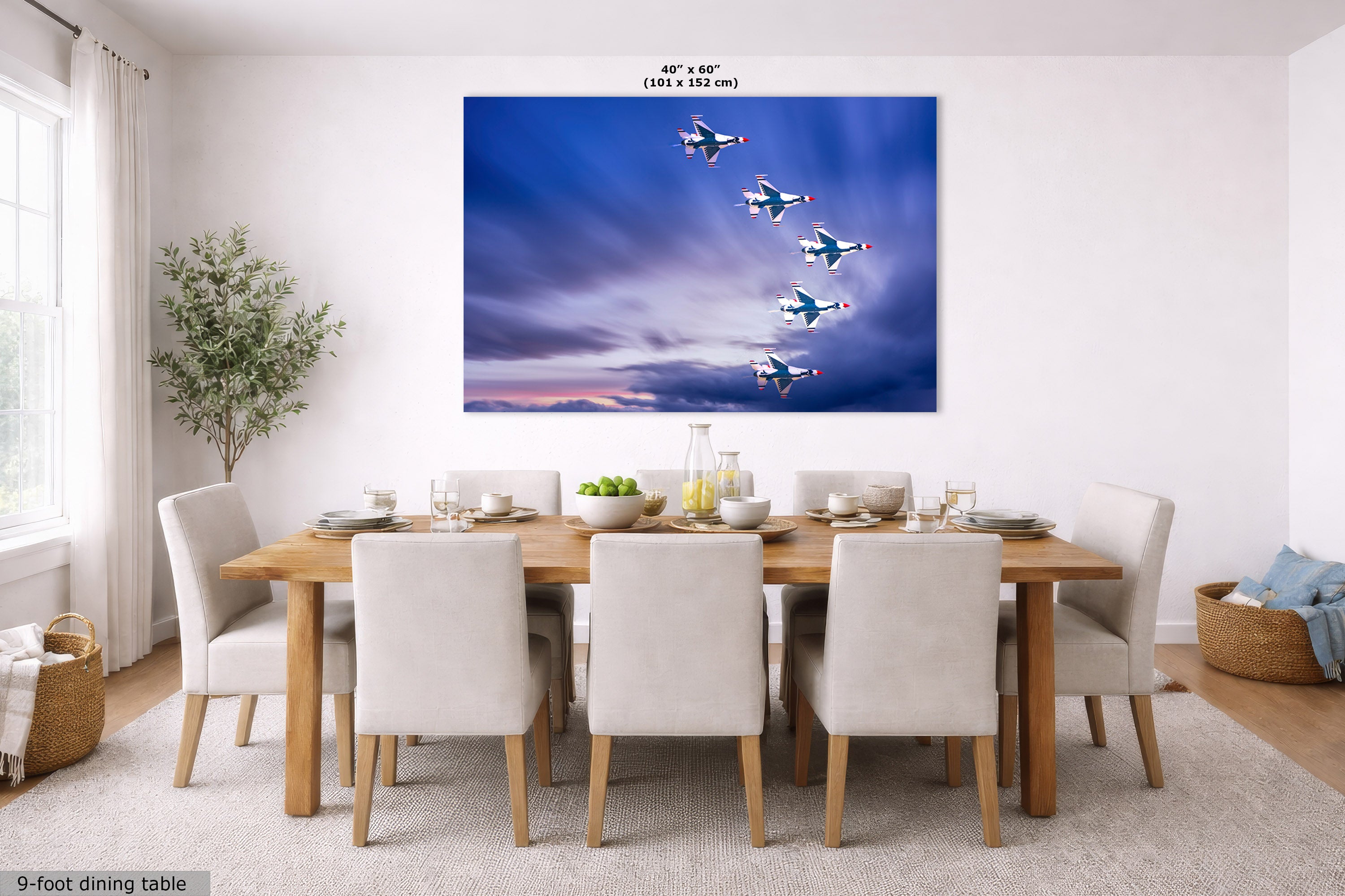 A large rectangular wall art print showing a formation of fighter jets flying through a dramatic blue and purple sky, displayed above a wooden dining table with white upholstered chairs in a bright modern dining room. Small text at the top reads 40 in x 60 in, and text at the bottom left reads 9-foot dining table.