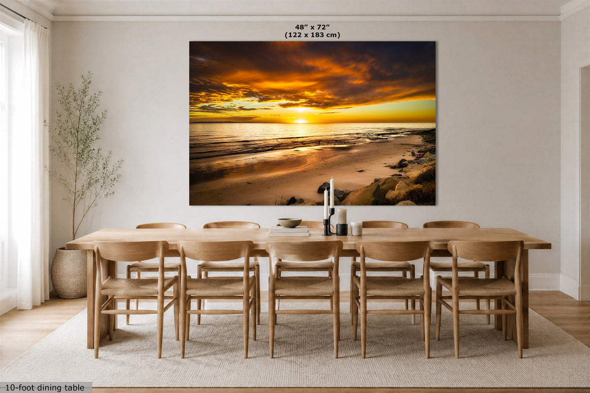 A large wall art print showing a dramatic beach sunset hangs above a wooden dining table and chairs in a bright, modern dining room. The print includes text at the top reading 48" x 72" (122 x 183 cm).