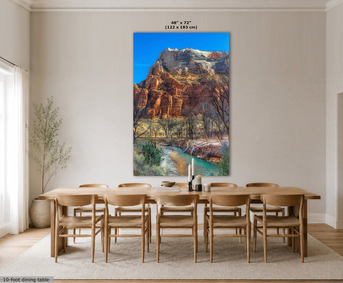 A large vertical wall art print showing a canyon landscape with red rock cliffs, a turquoise river, and blue sky, displayed above a wooden dining table and chairs in a bright neutral dining room. Text at the top reads 48 x 72" (122 x 183 cm), and a small note at bottom left says 10-foot dining table.