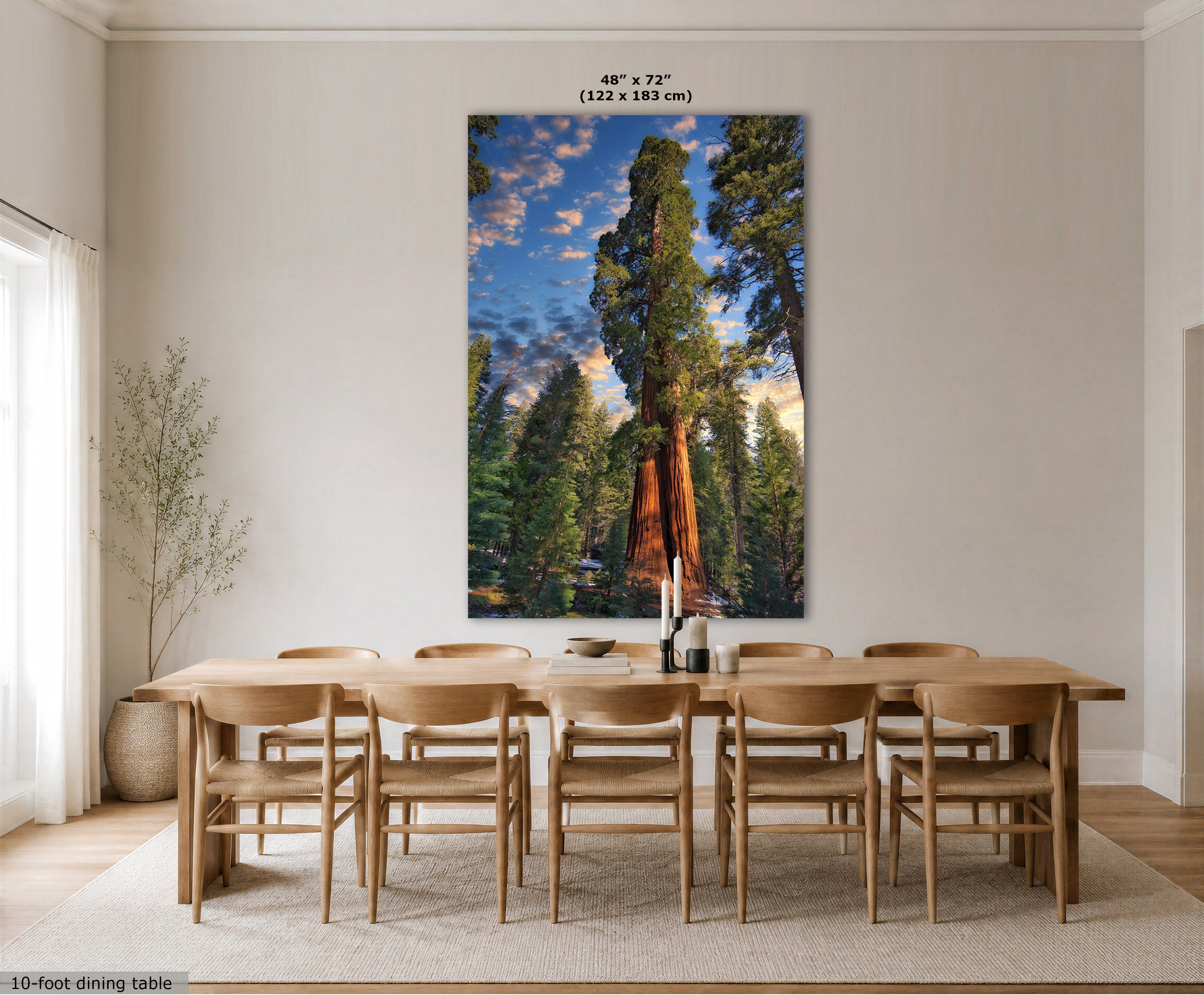 A large vertical wall art print depicting a giant sequoia tree in a forest under a blue sky, displayed above a wooden dining table and chairs in a bright, modern dining room. The print includes size text at the top and a small label at the bottom left.