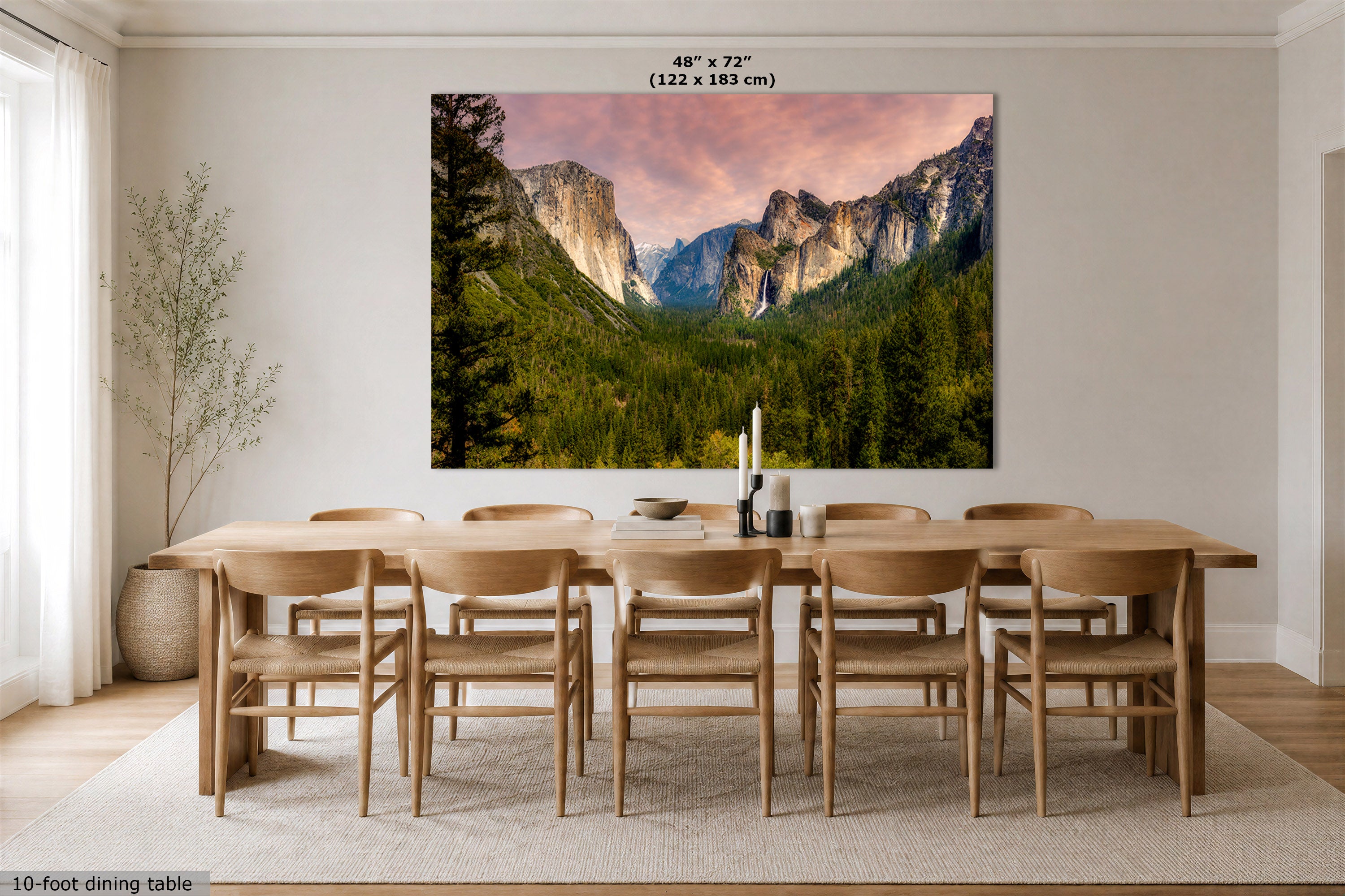 A large wall art print showing a mountain valley landscape with green trees and a pink sky, displayed above a wooden dining table and chairs in a bright dining room. Text at the top reads 48" x 72" (122 x 183 cm), and text at the bottom left says 10-foot dining table.