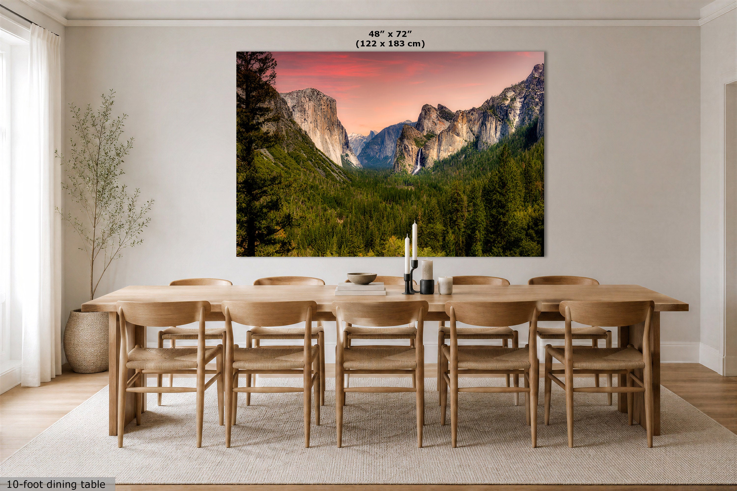 A large wall art print showing a mountain valley landscape with green trees and a pink-orange sky, displayed above a wooden dining table and chairs in a bright dining room. Text at the top reads 48" x 72" (122 x 183 cm), and a small note at bottom left says 10-foot dining table.