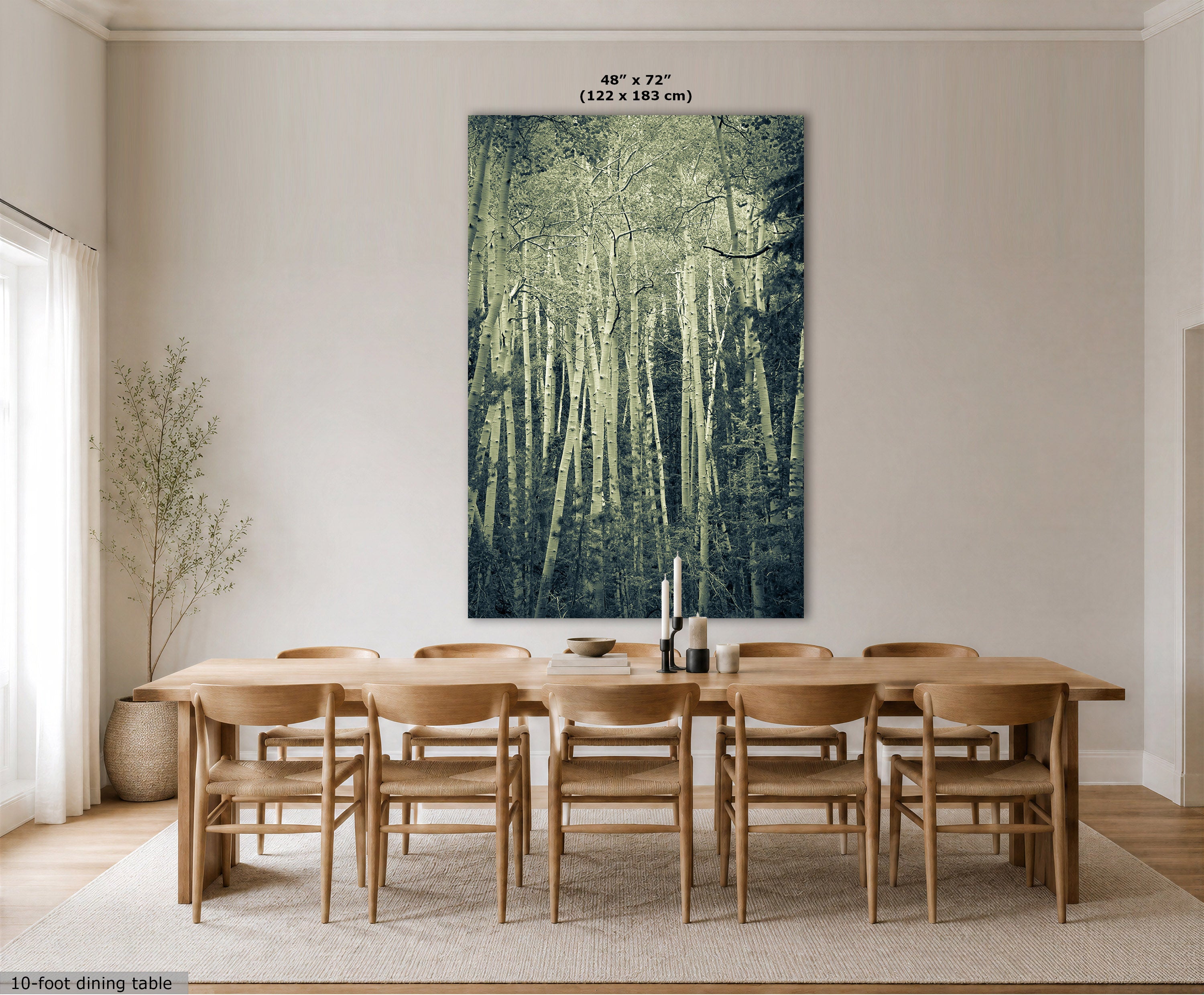 A large vertical wall art print showing a forest of slender trees in muted green and blue tones, displayed above a wooden dining table and chairs in a bright neutral dining room. Small text at the top reads 48" x 72" (122 x 183 cm), and a small caption at the bottom left says 10-foot dining table.