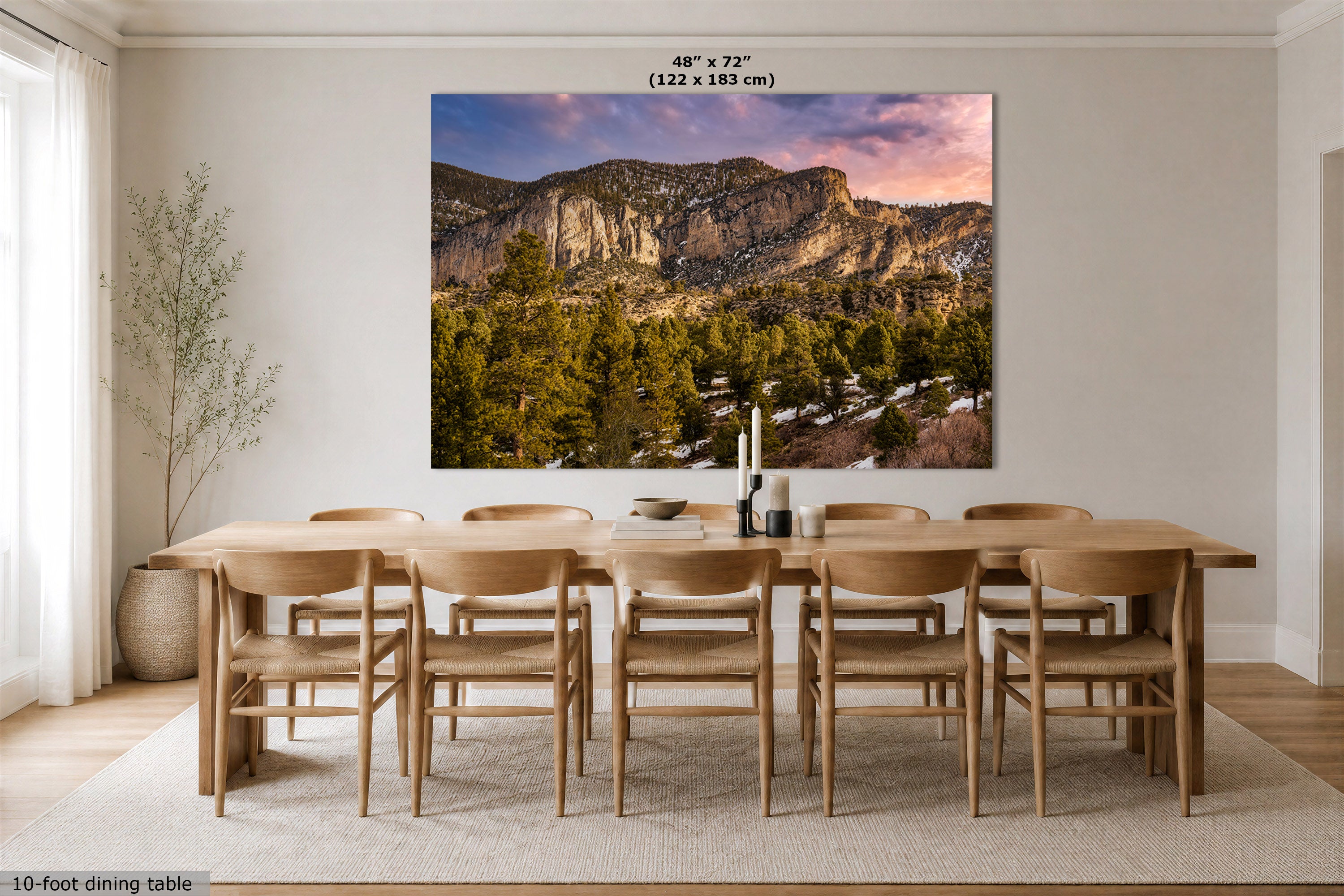 A large rectangular wall art print showing a mountain landscape with trees and a pink-purple sky, displayed above a wooden dining table and chairs in a bright dining room. Text at the top reads 48" x 72" (122 x 183 cm).