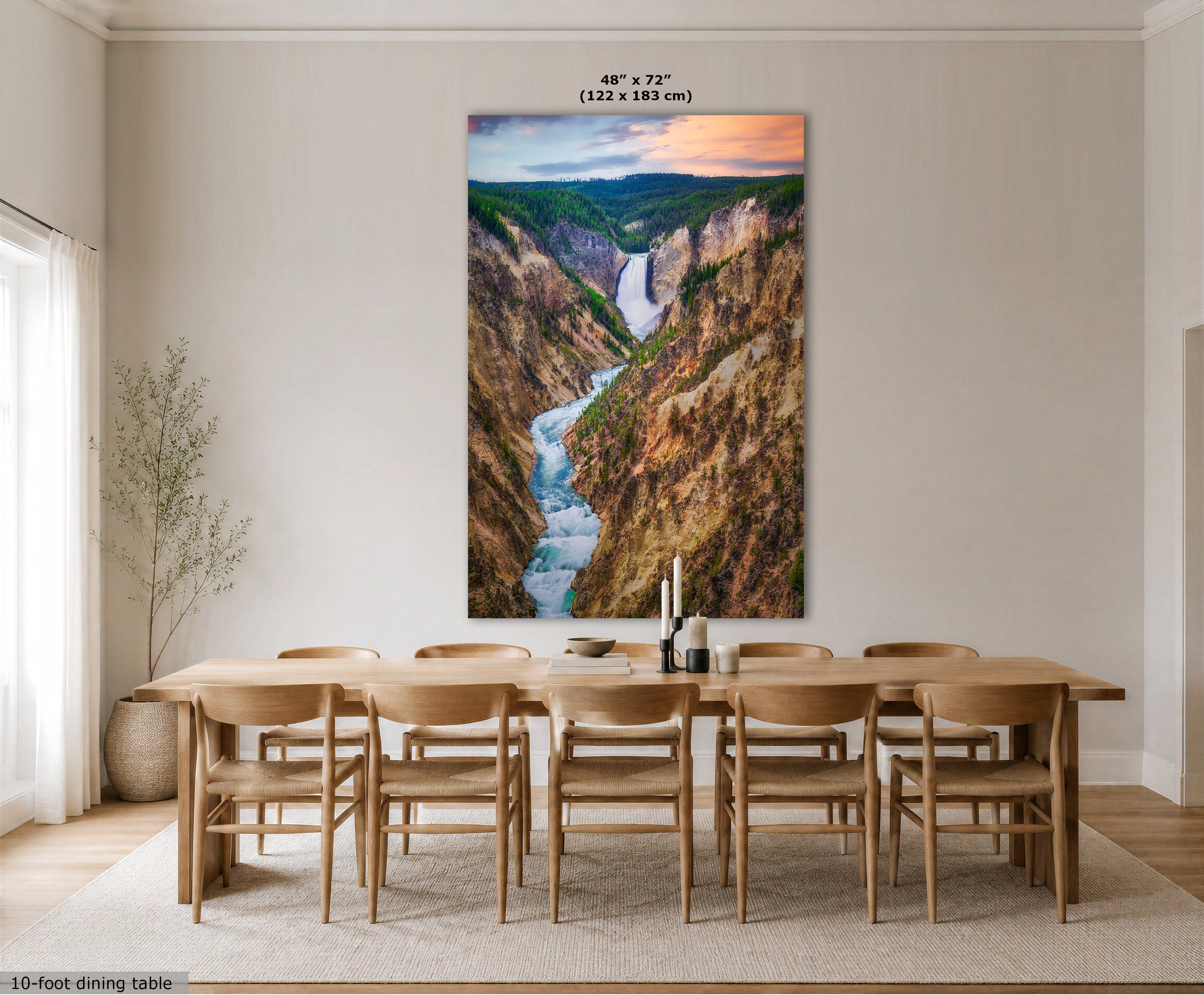 A large vertical wall art print showing a deep canyon with a rushing river and a waterfall under a sunset sky, displayed above a wooden dining table and chairs in a bright modern room. Text at the top indicates the print size as 48 x 72 inches (122 x 183 cm).