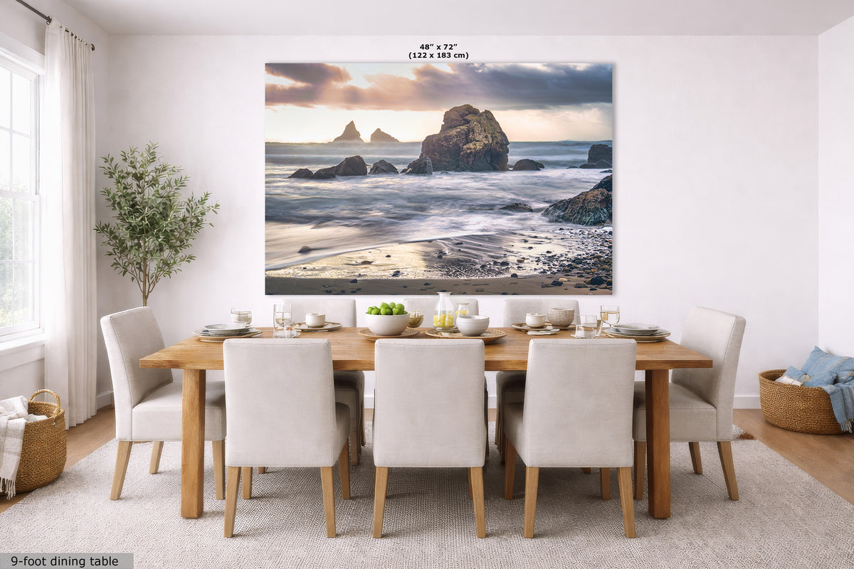 A large wall art print depicting a rocky beach and ocean scene, displayed in a bright dining room above a wooden dining table with white chairs. The print has a small size label at the top reading 48" x 72" (122 x 183 cm).