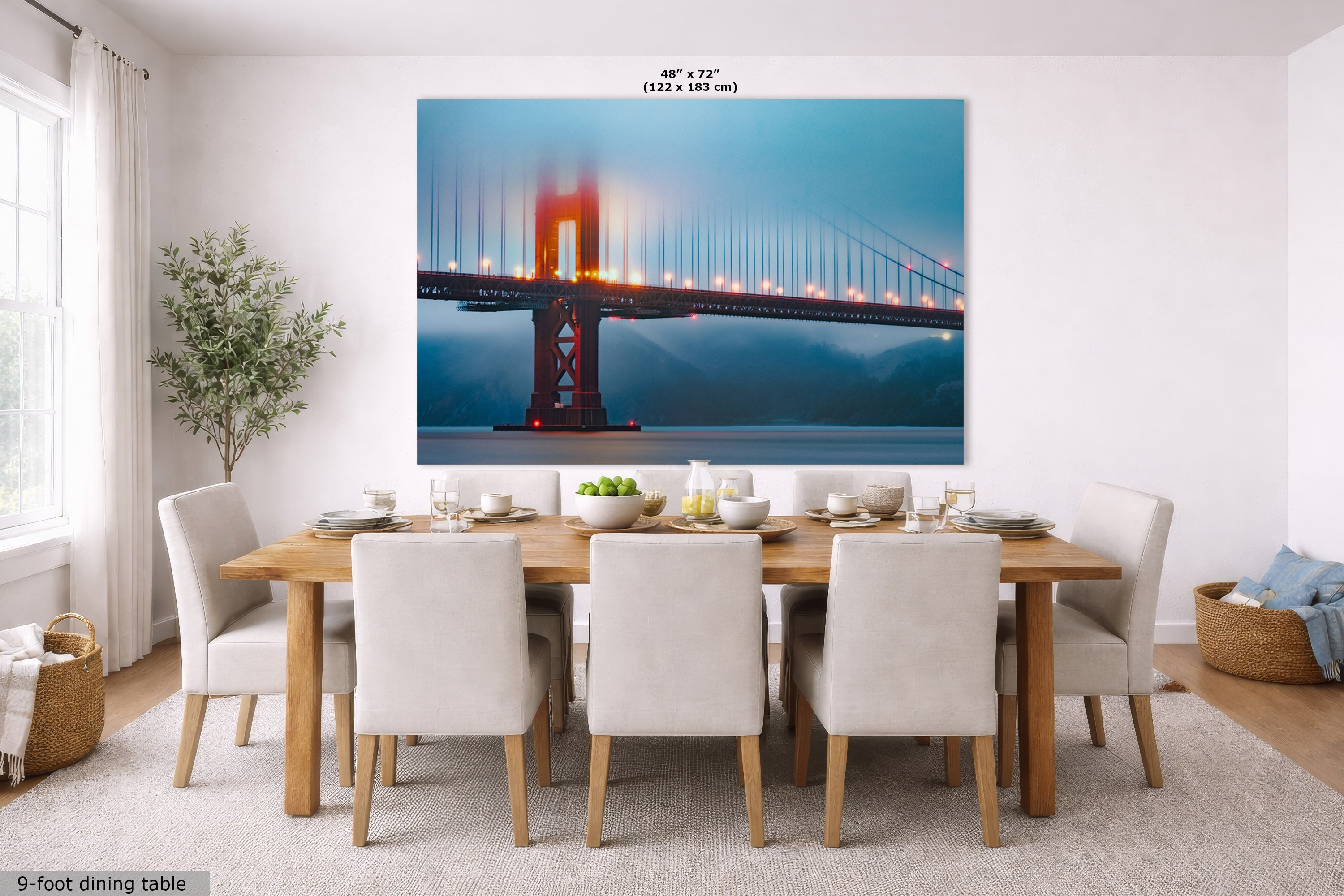 A large wall art print of the Golden Gate Bridge displayed above a 9-foot dining table in a bright, modern dining room. The print features the iconic orange-red bridge against a blue sky, and the text '48" x 72" (122 x 183 cm)' is visible at the top of the print.