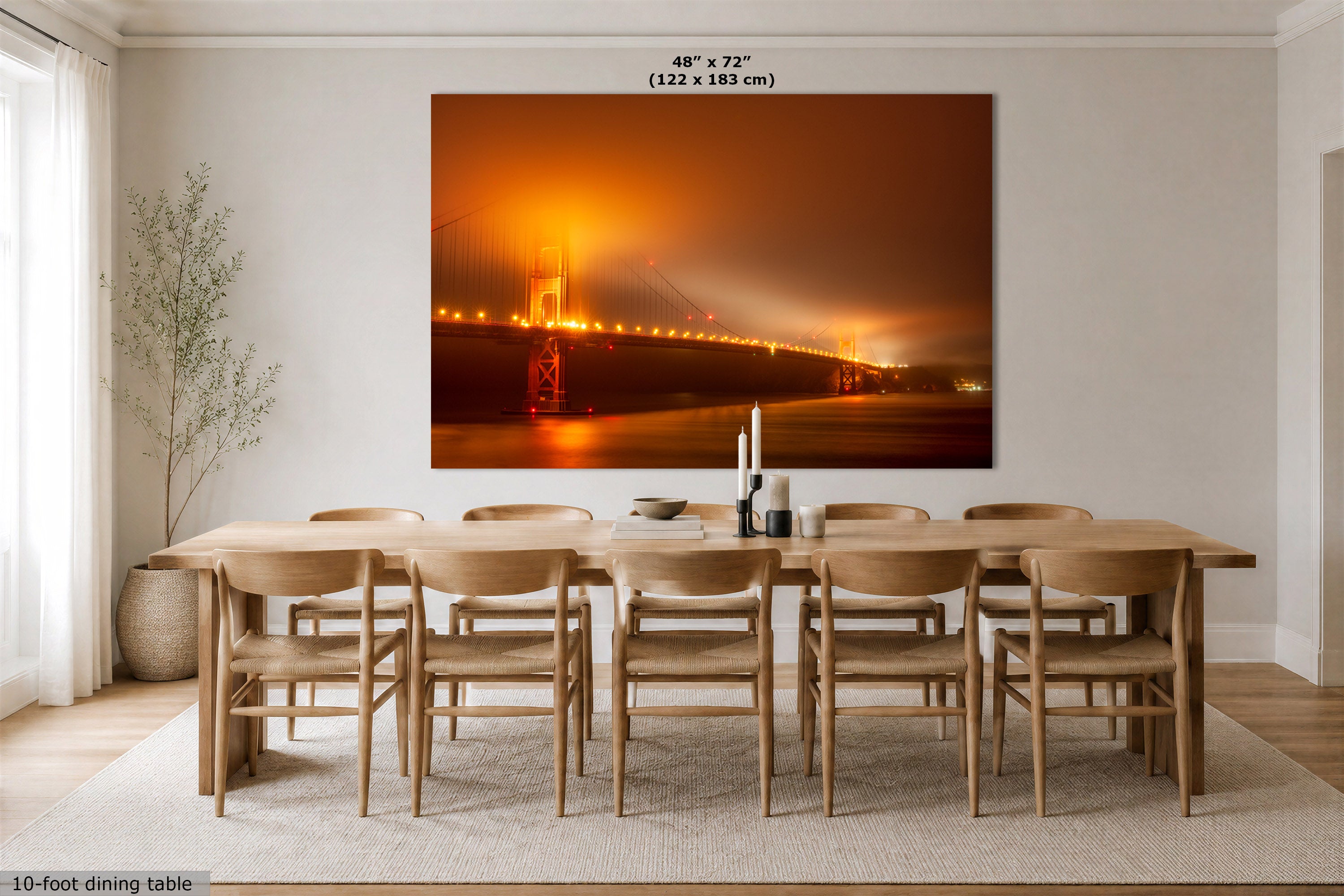 A large rectangular wall art print showing a glowing orange suspension bridge over water at dusk, displayed above a wooden dining table and chairs in a bright modern room. Small text at the top reads 48 x 72" (122 x 183 cm), and a 10-foot dining table is shown below for scale.