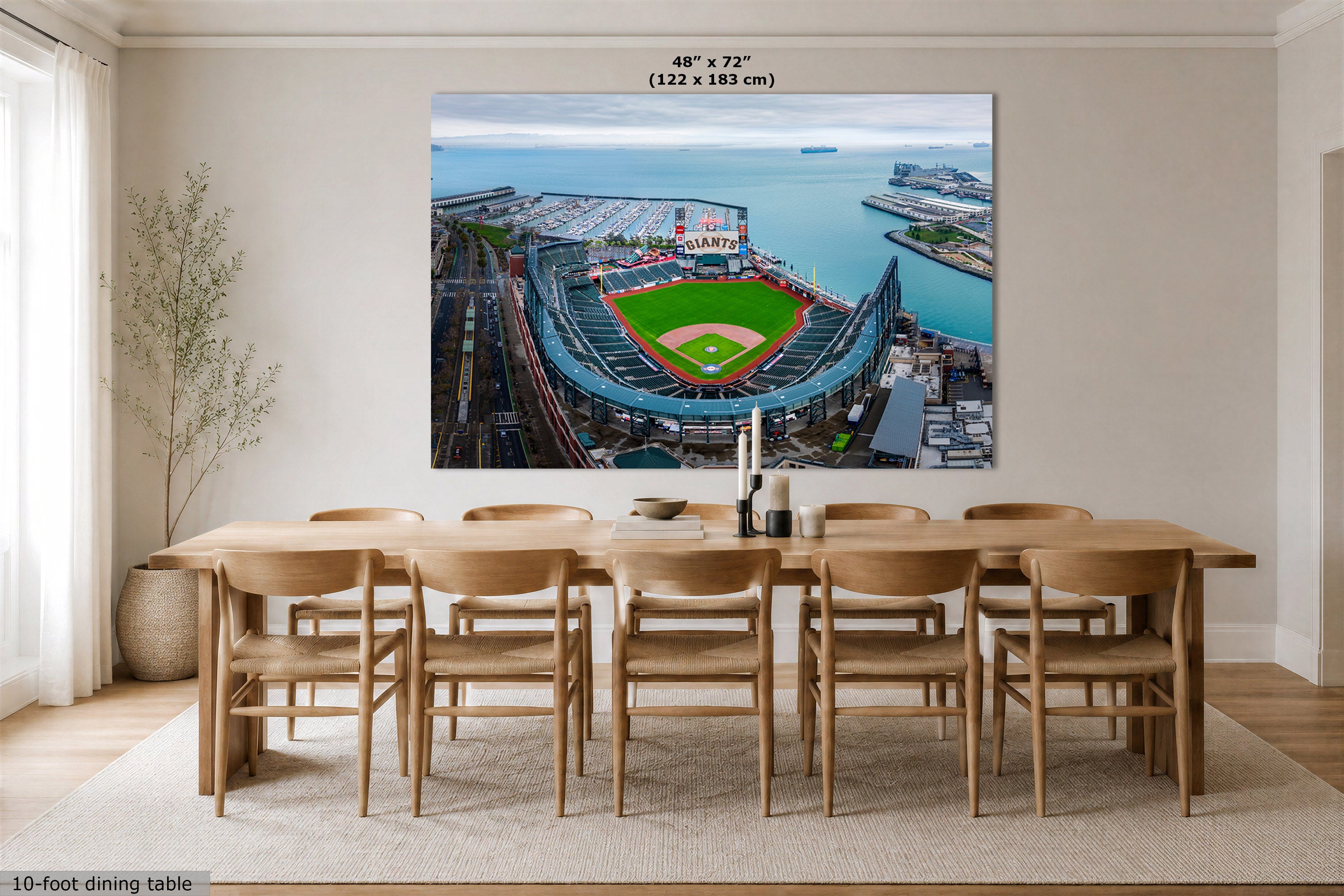 A large Oracle Park marina wall art print showing an aerial view of a baseball stadium and San Francisco Bay, displayed above a wooden dining table in a bright modern room. Text at the top reads 48" x 72" (122 x 183 cm), and text at the bottom left says 10-foot dining table.
