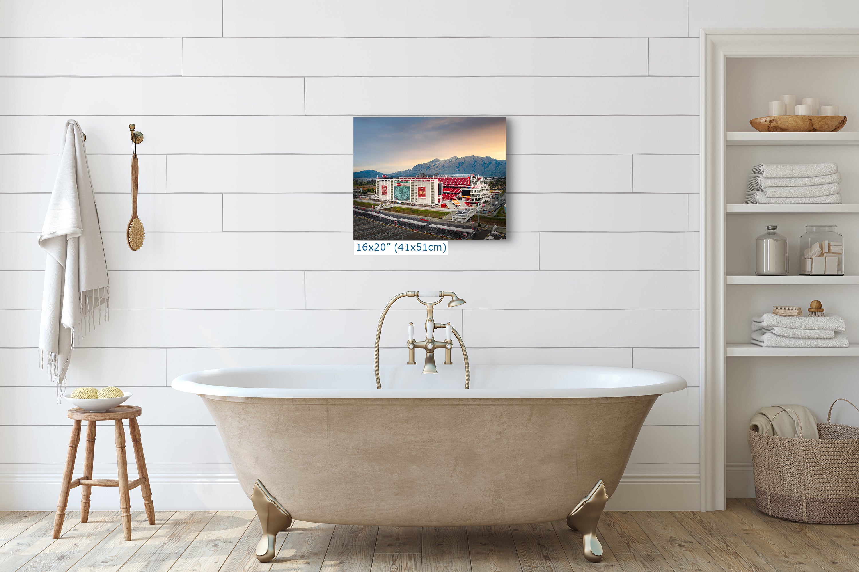 a bathroom with a clawfoot bathtub, a wooden stool, and a shelf with various toiletries. Above the bathtub, there is a framed photograph of a building with a red roof and a mountain in the background.