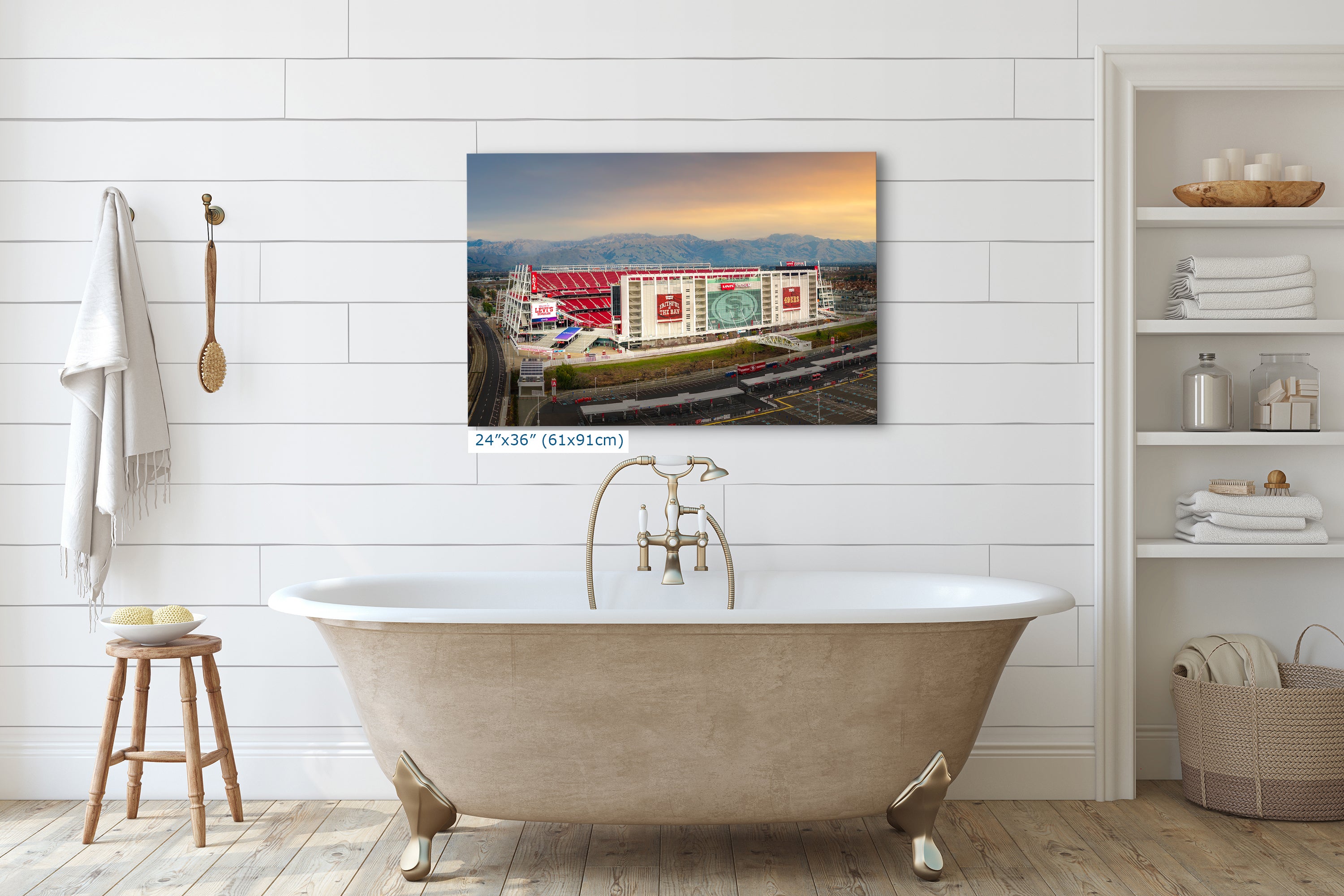 a large, white, clawfoot bathtub in a bathroom setting, with a large framed picture of a stadium or sports venue hanging on the wall above it.