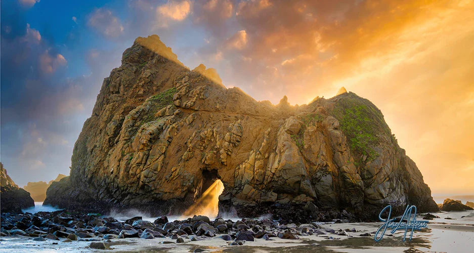 The majestic Keyhole Arch in Big Sur stands against a sunset, its silhouette framed by a golden sky, embodying the timeless allure of California's rugged coastline.