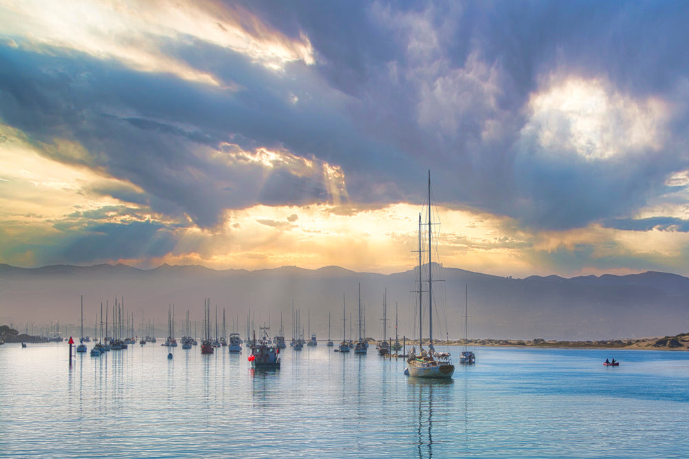 Coastal wall art of a marina with sailboats under a dramatic sky with sunbeams, available as limited edition art prints.