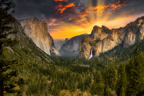 Stunning photograph of Tunnel View in Yosemite National Park featuring majestic El Capitan on the left, the iconic Bridalveil Fall on the right, and the captivating Half Dome in the background under a vibrant sunset sky.