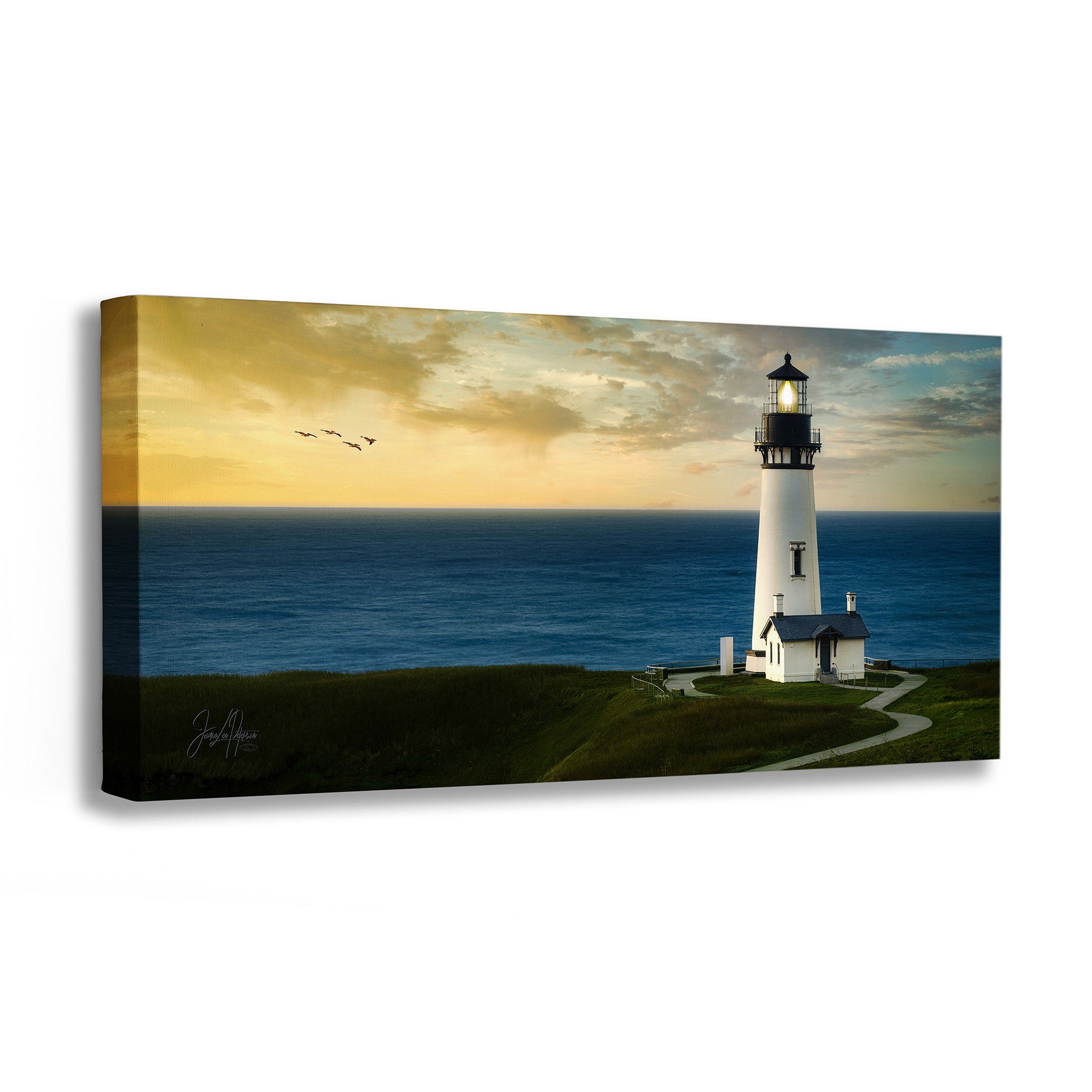 A rectangular canvas wall art print showing a white lighthouse on a grassy cliff overlooking a blue ocean under a warm sunset sky, photographed against a plain white background.