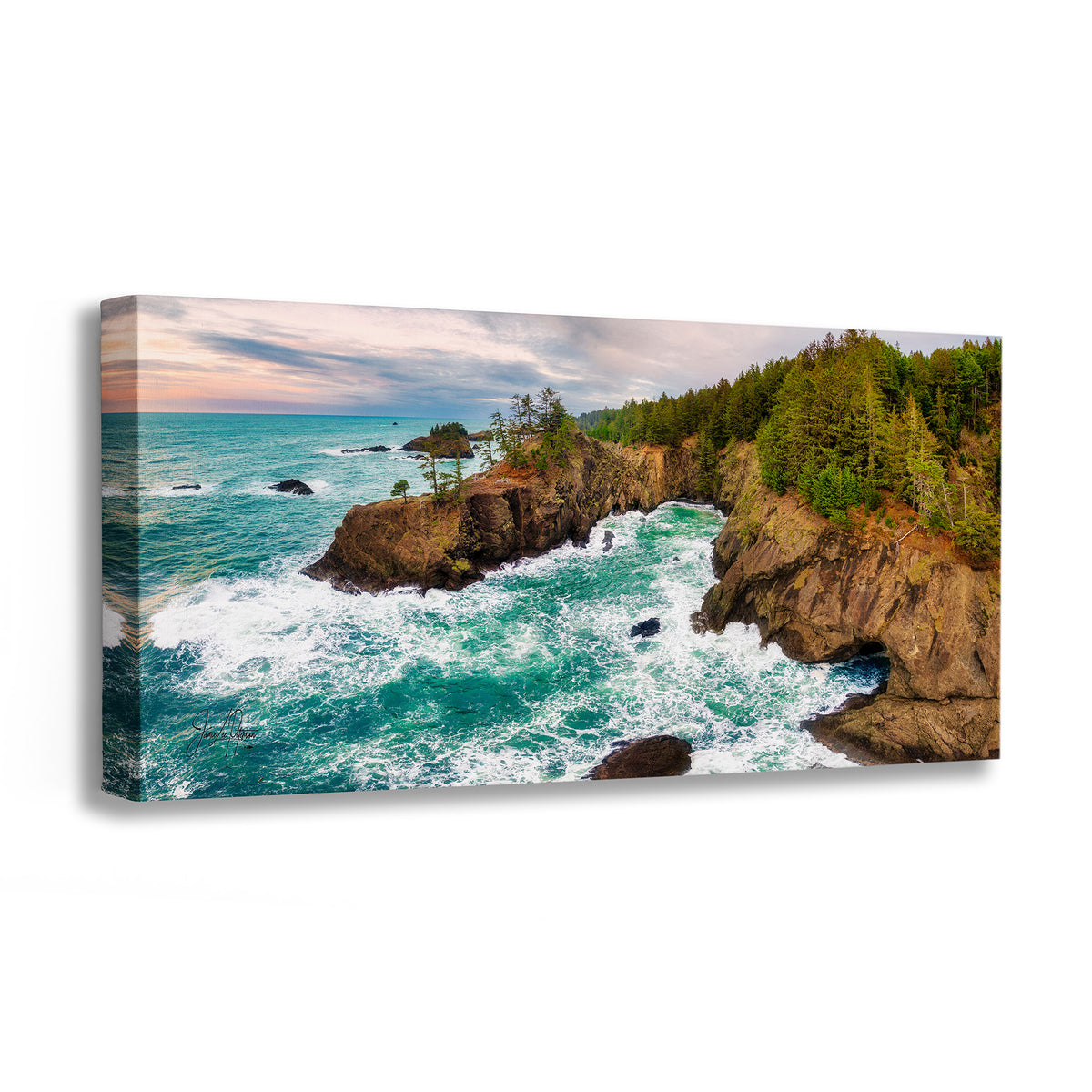 A rectangular canvas wall art print showing a coastal rocky shoreline with turquoise ocean water, white surf, green trees, and a cloudy sky, photographed against a plain white background.
