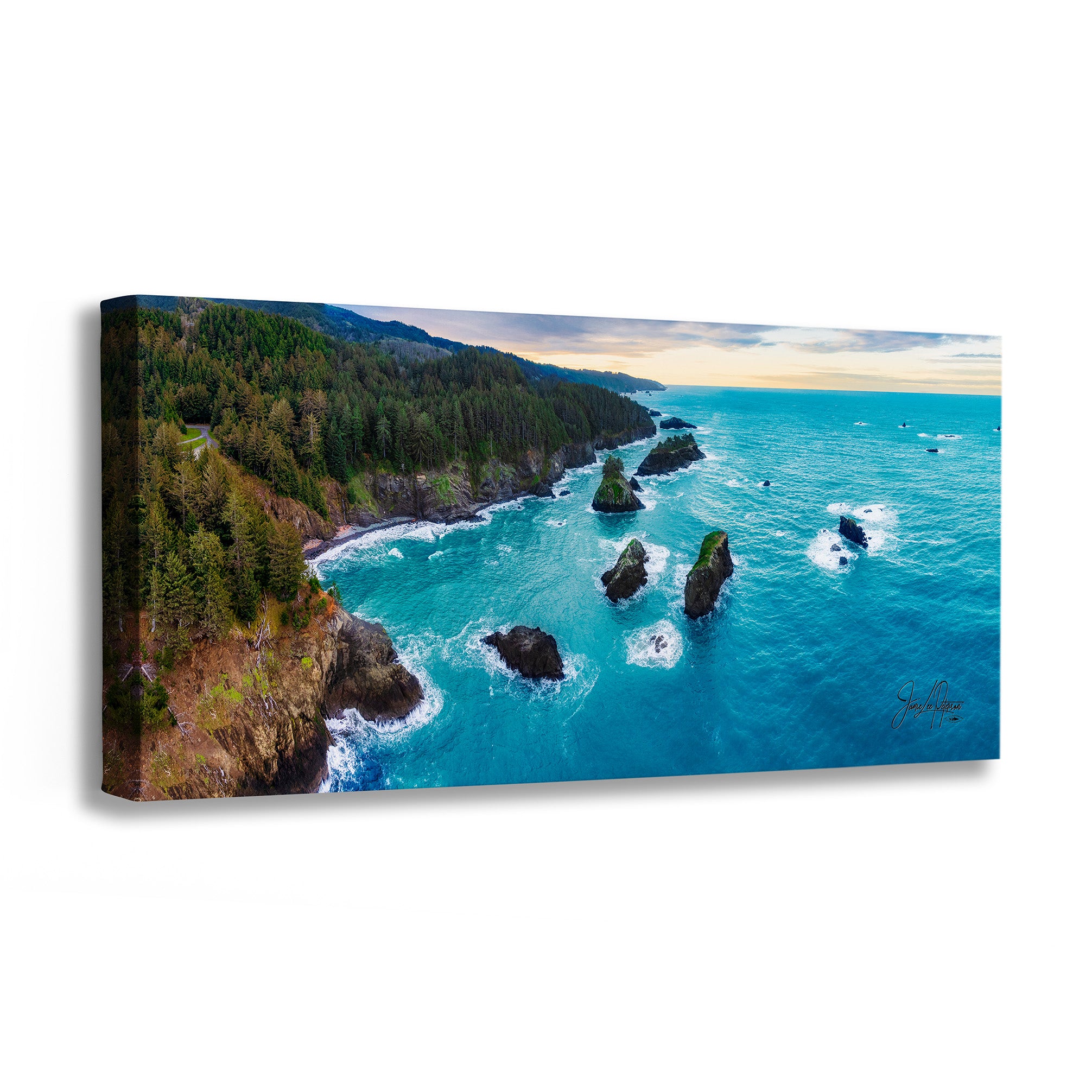 A panoramic canvas wall art print depicting an aerial view of a coastal landscape with turquoise ocean water, sea stacks, a forested cliff, and a pale sky. The canvas is shown at an angle against a plain white background.