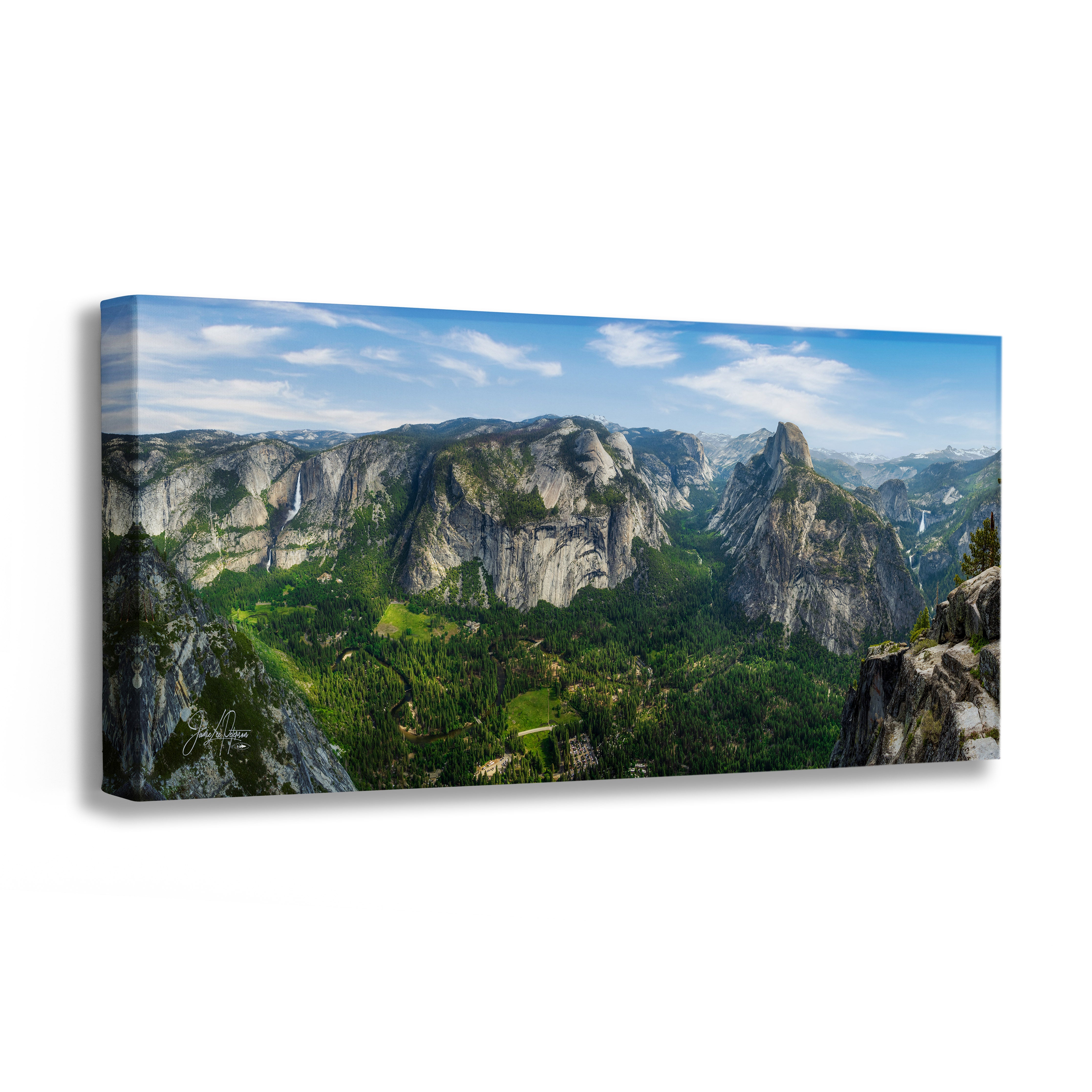 A panoramic canvas wall art print depicting a lush green Yosemite National Park showing Yosemite Falls, Half Dome, and Nevada Falls from Glacier Point. It has a mountain valley with steep rocky cliffs under a blue sky with light clouds, shown at a three-quarter angle on a white background.