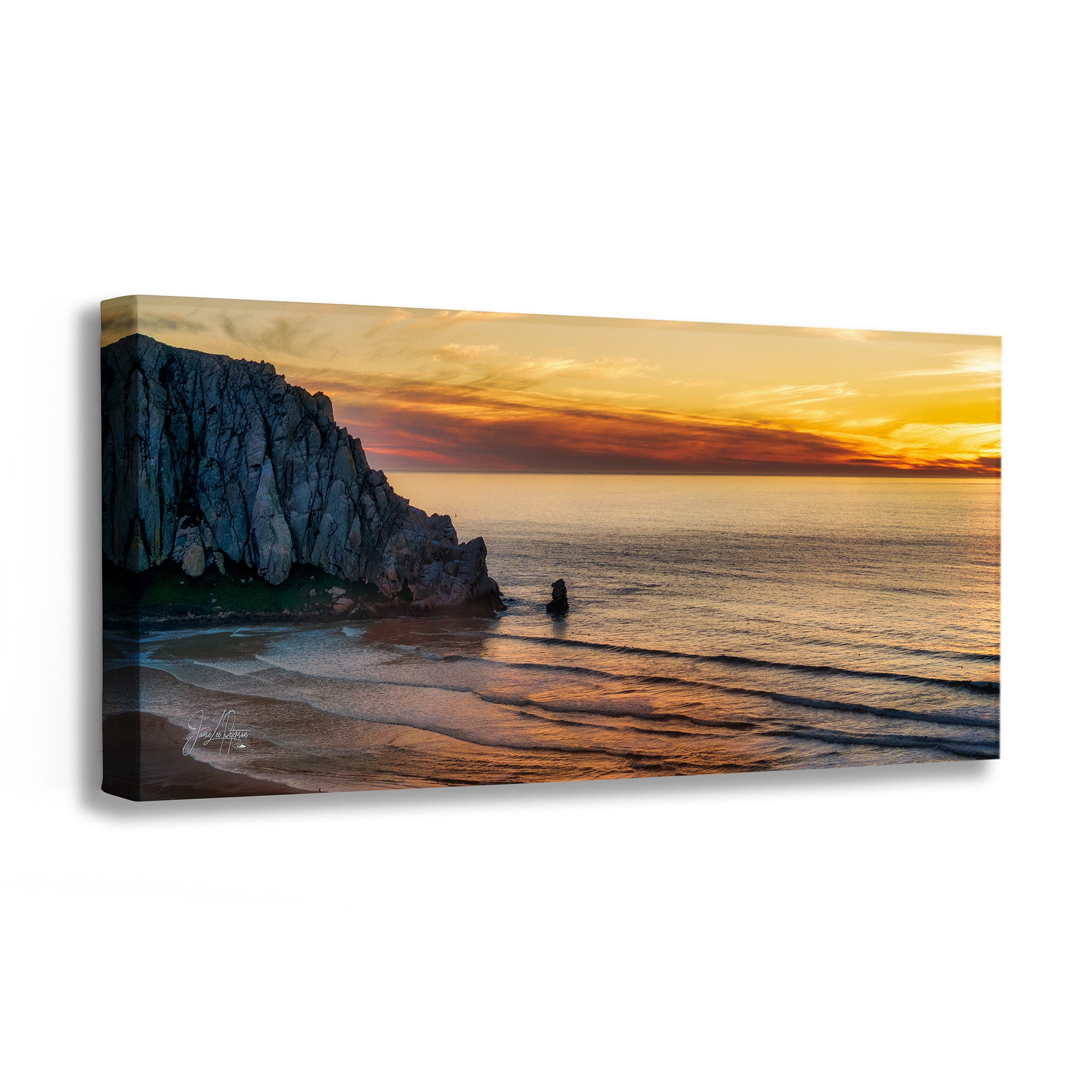 A panoramic canvas wall art print depicting a dramatic rocky coastline at sunset over calm ocean water, shown at a slight angle against a plain white background.