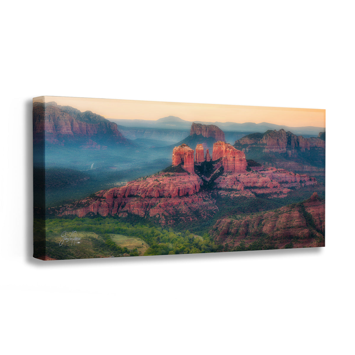 A canvas wall art print depicting Cathedral Rock, a desert canyon landscape in Sedona, Arizona, with red rock formations, green valley vegetation, and misty blue mountains in the distance, photographed against a plain white background.