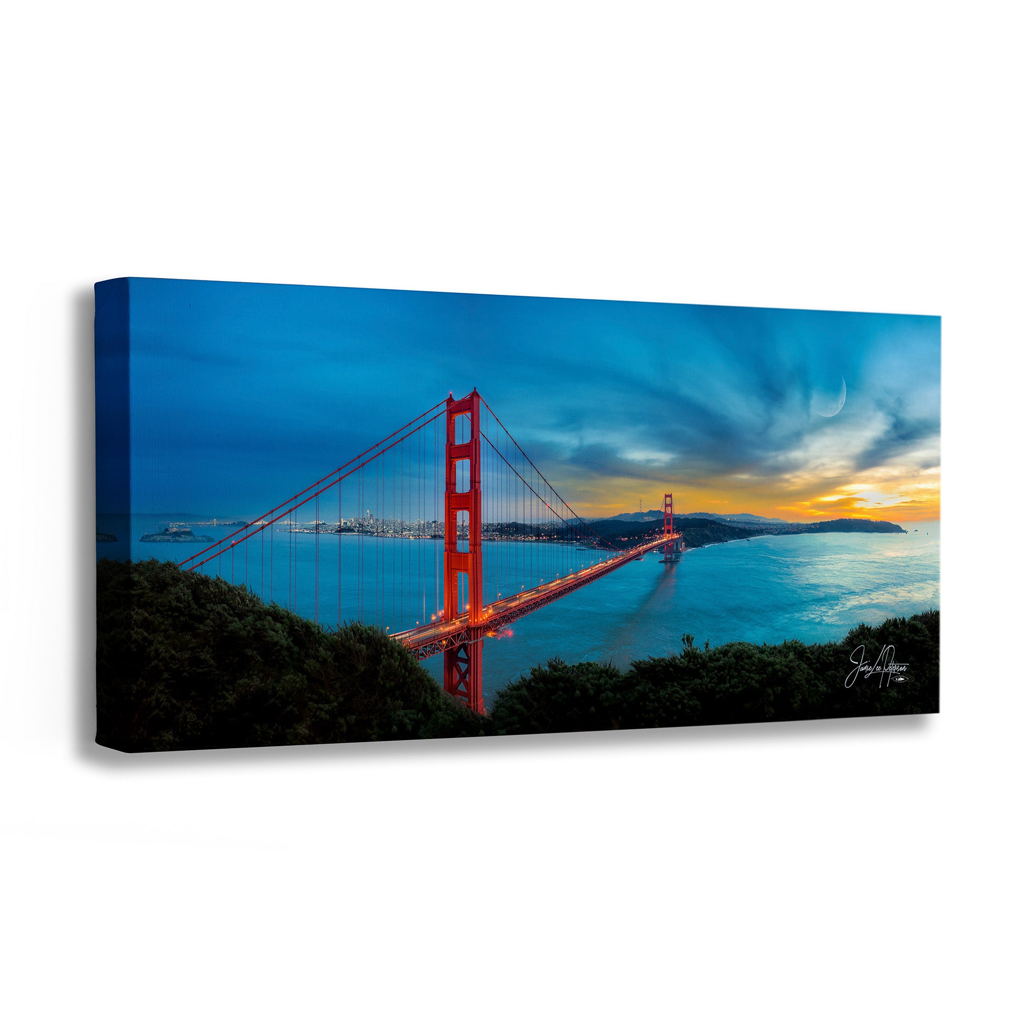 A rectangular canvas wall art print showing the Golden Gate Bridge over water at dusk, with a blue sky, warm sunset glow on the horizon, and dark foreground silhouettes. The canvas is photographed at a slight angle against a clean white background.