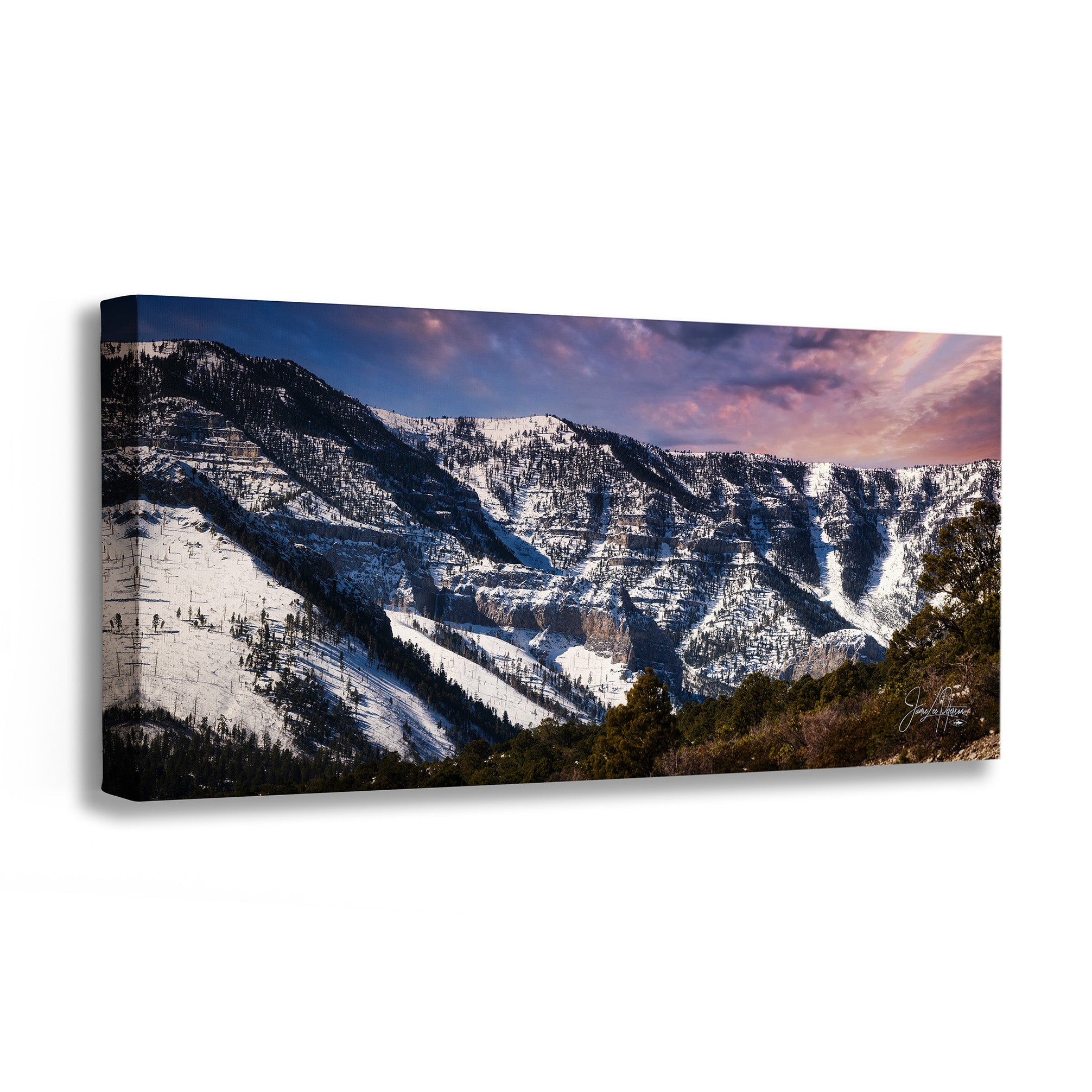 A panoramic canvas wall art print depicting a snow-covered mountain range under a dramatic pink and blue sunset sky, shown at an angle on a white background.