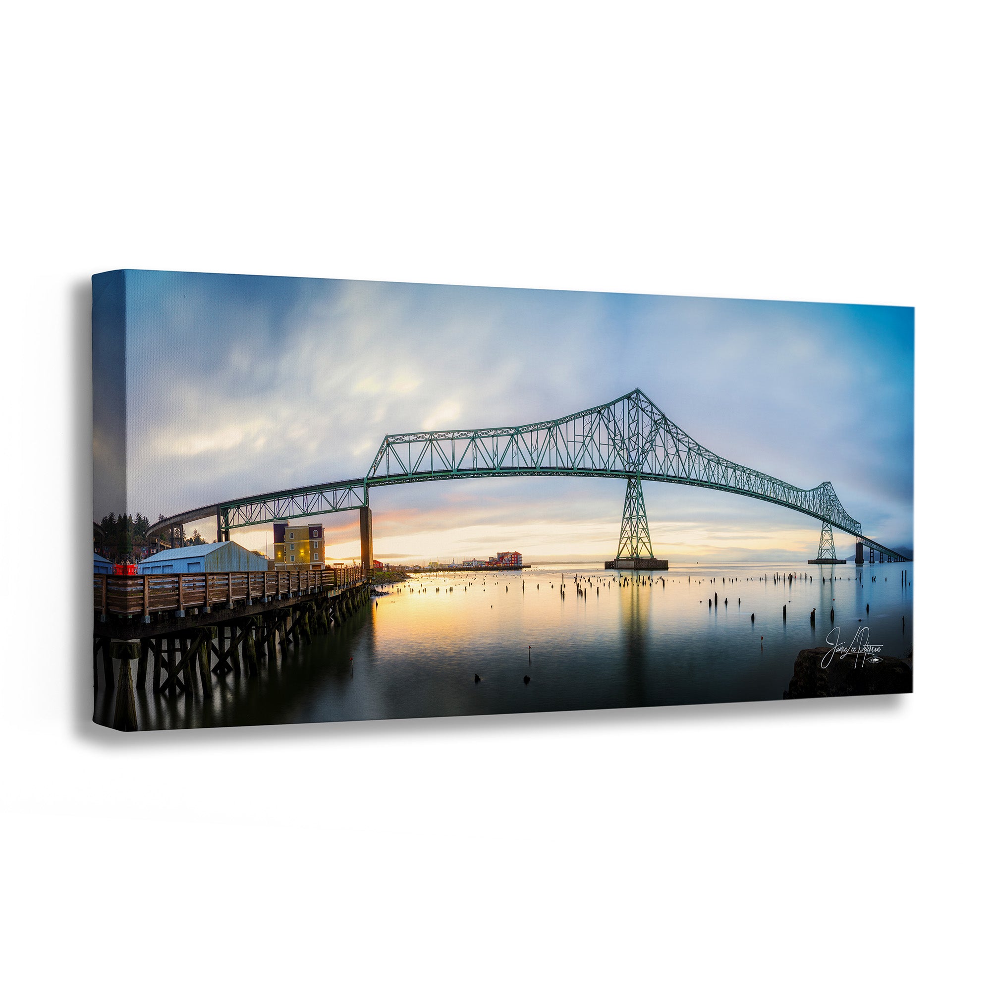 A rectangular canvas wall art print showing a long bridge spanning calm water at sunset, photographed against a plain white background with a slight shadow.