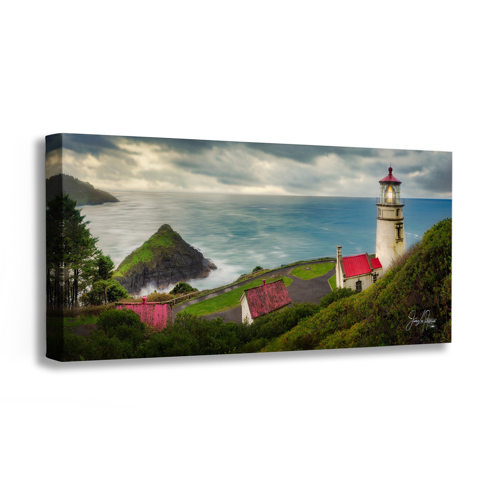 A rectangular canvas wall art print showing a coastal lighthouse scene with ocean, rocky shoreline, trees, and small buildings with red roofs, photographed against a plain white background.