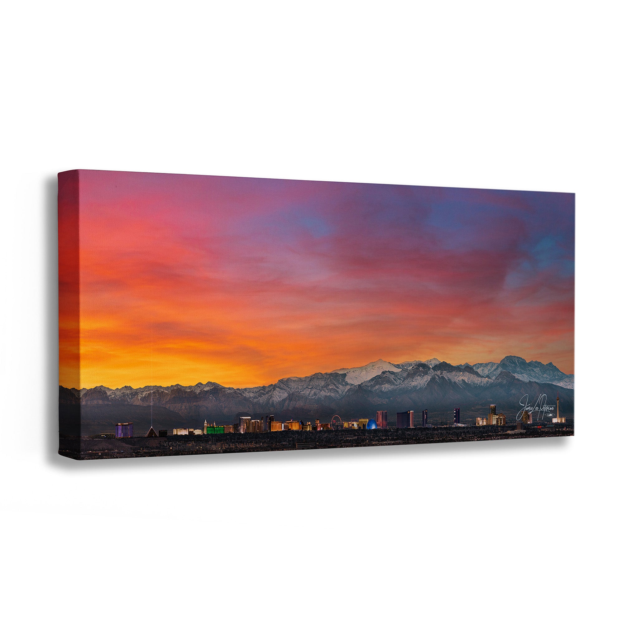 A panoramic canvas wall art print depicting a colorful sunset over a mountain range and a small city skyline, shown at an angle against a white background.