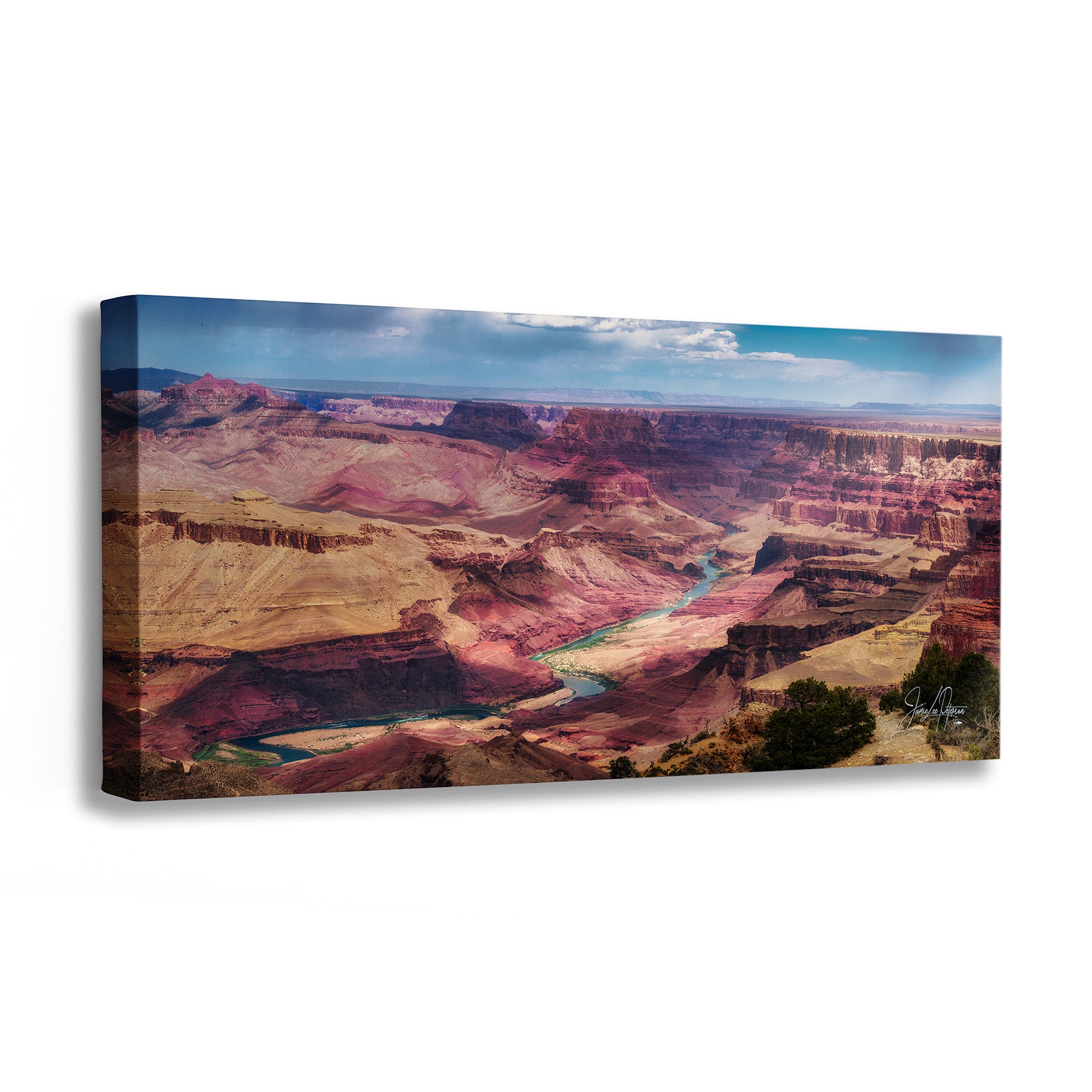 A rectangular canvas wall art print showing a canyon landscape with layered red, brown, and tan rock formations, a winding river, and a blue sky with clouds. The canvas is photographed at an angle against a plain white background.